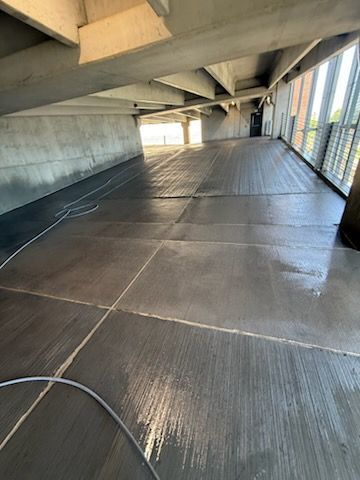 Covered walkway with concrete beams, metal fencing, and wet floor reflecting light