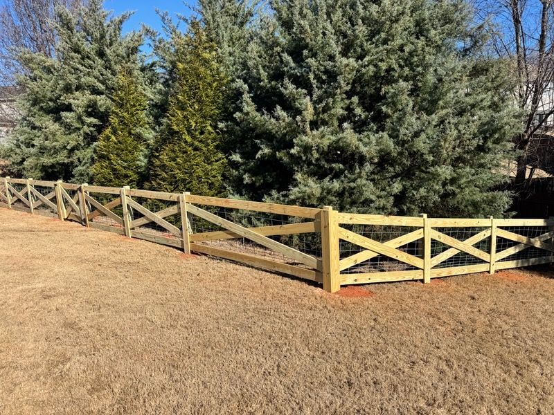 Wooden fence with criss-cross design, bordering a yard with dry grass and evergreen trees.