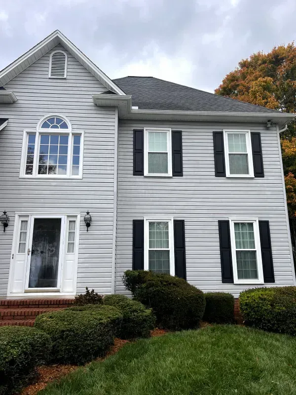 Two-story house with gray siding, black shutters, and a dark roof under a cloudy sky.
