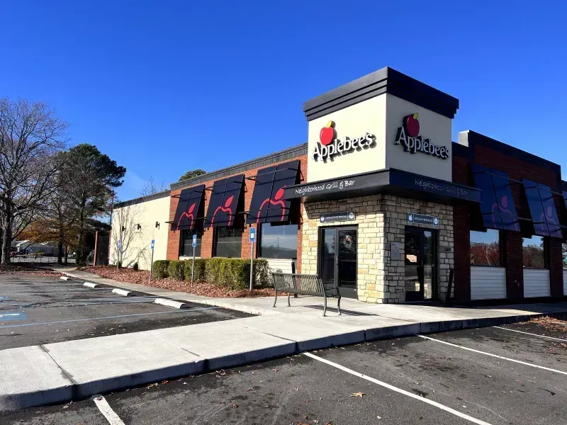 Applebee's restaurant exterior with black awnings, red apple logo, stone accents, and blue sky.