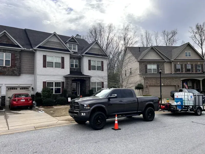A dark gray pickup truck parked on a street in front of two-story houses; a trailer with equipment is attached.