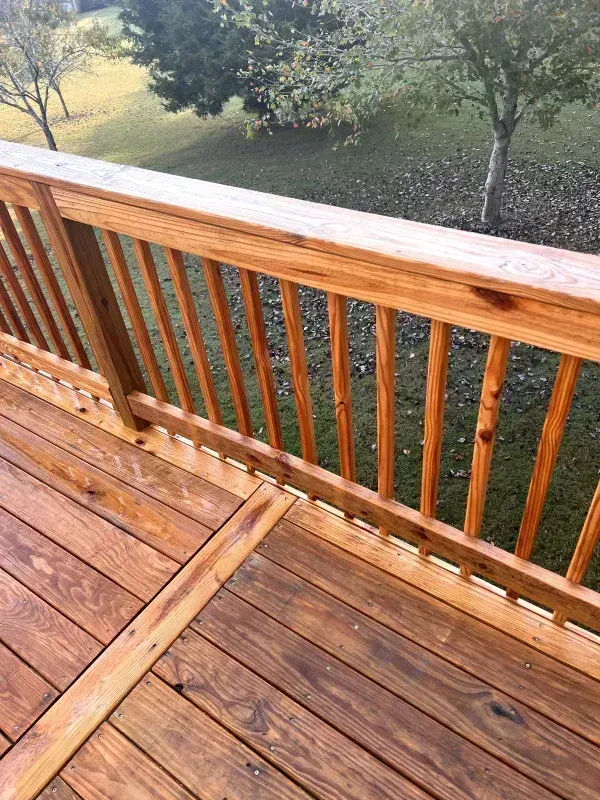 Wooden deck with railing, stained brown, overlooking a grassy yard with trees.