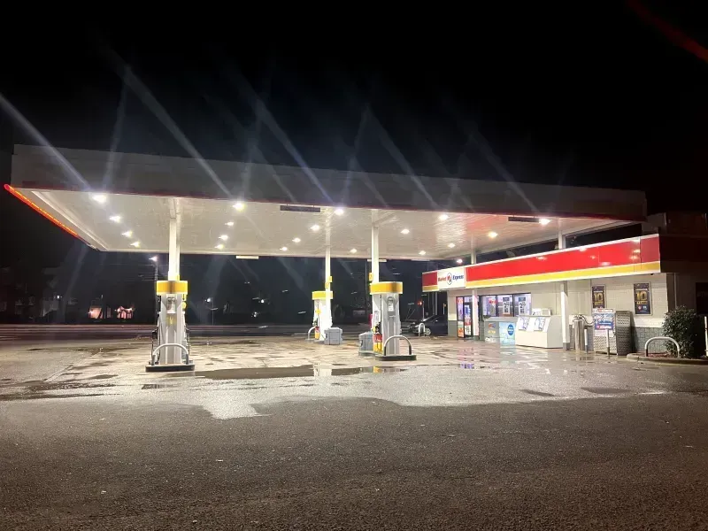 Gas station at night with bright lights illuminating pumps and a convenience store.