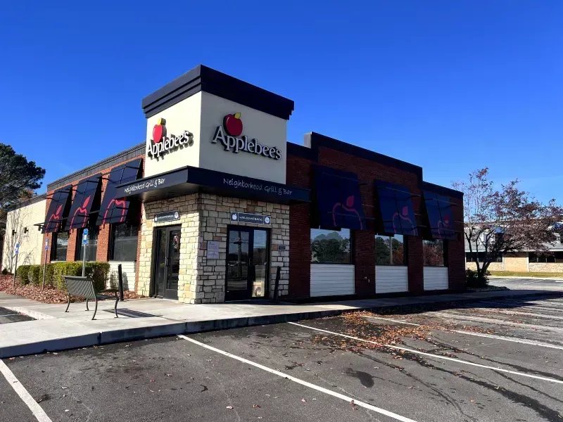 Applebee's restaurant exterior on a sunny day; brick, stone, and black awning; empty parking lot.