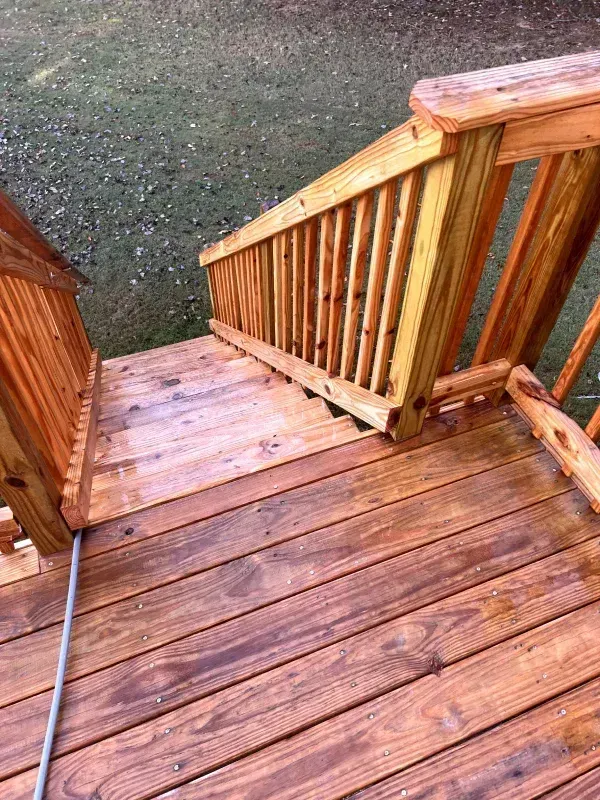 Wooden deck and stairs with railing, stained brown, leading down to grass.