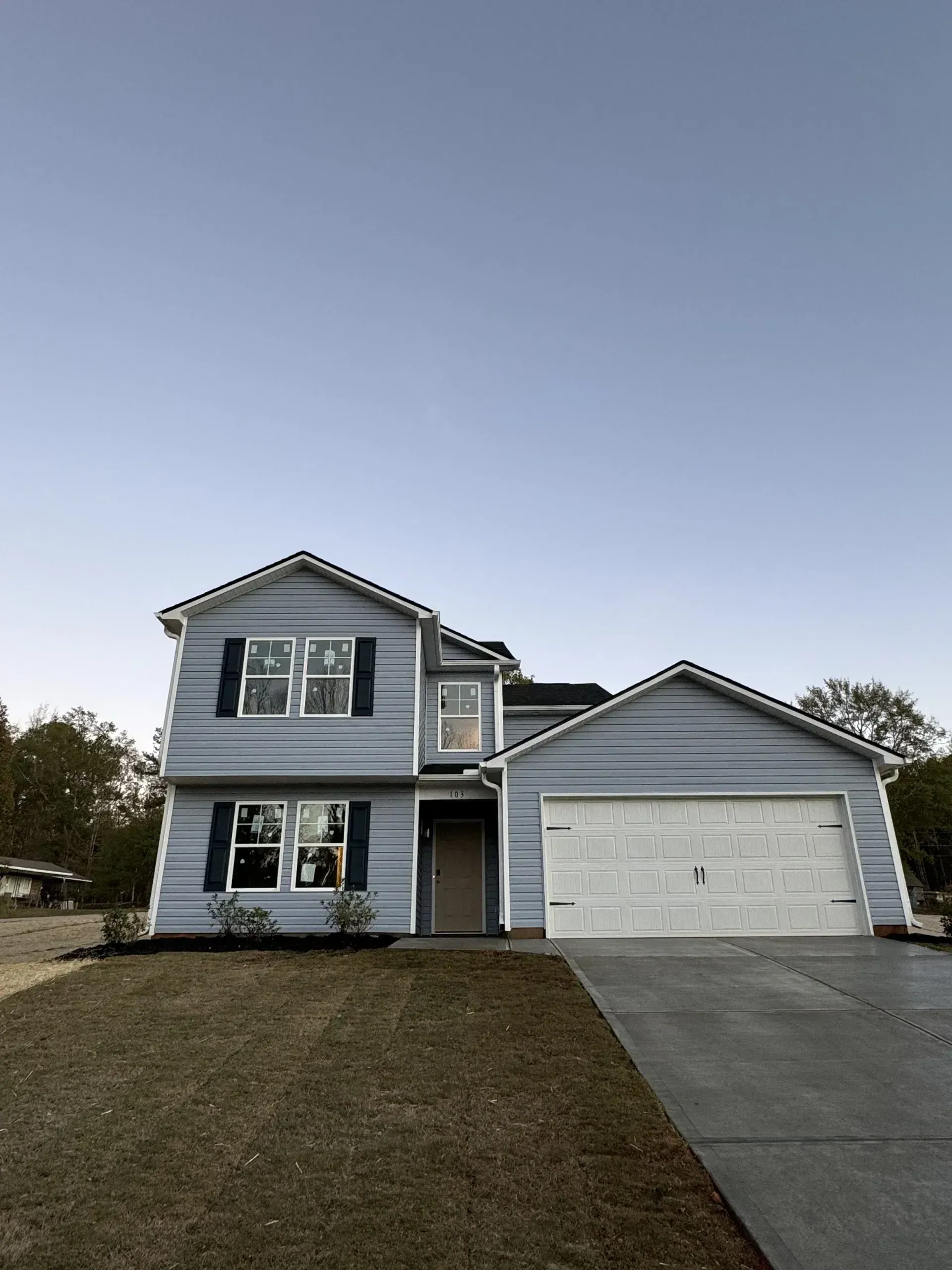 Blue two-story house with a garage and driveway on a grassy lawn under a clear sky.