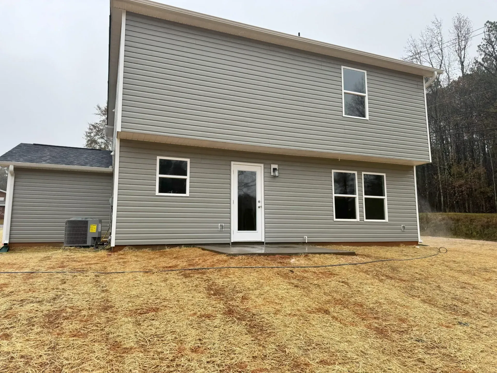 Back of a two-story gray house with multiple windows and a back door, set on a brown, grassy lawn.