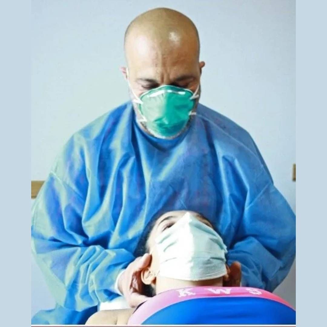 Trabajador sanitario con traje protector azul y mascarilla atendiendo a un paciente tumbado.