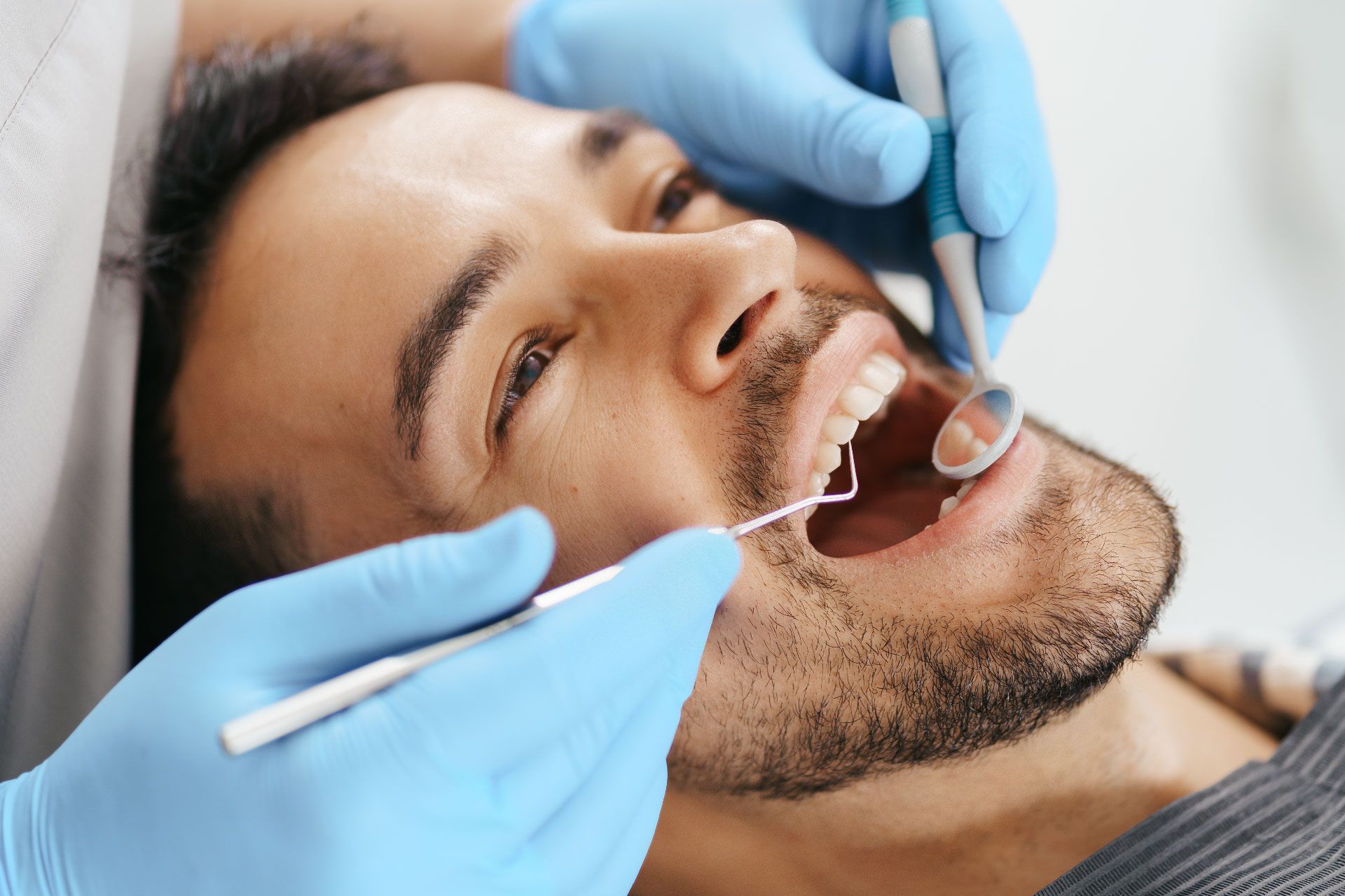 Dentista examinando los dientes de un paciente con un espejo y un instrumento dental, usando guantes azules.
