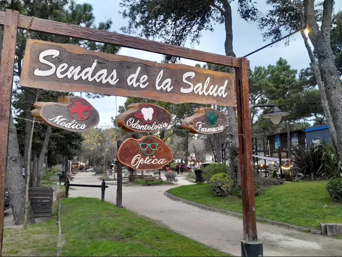 Un cartel de madera con la inscripción “Sendas de la Salada” se alza sobre un sendero del parque con árboles y edificios.