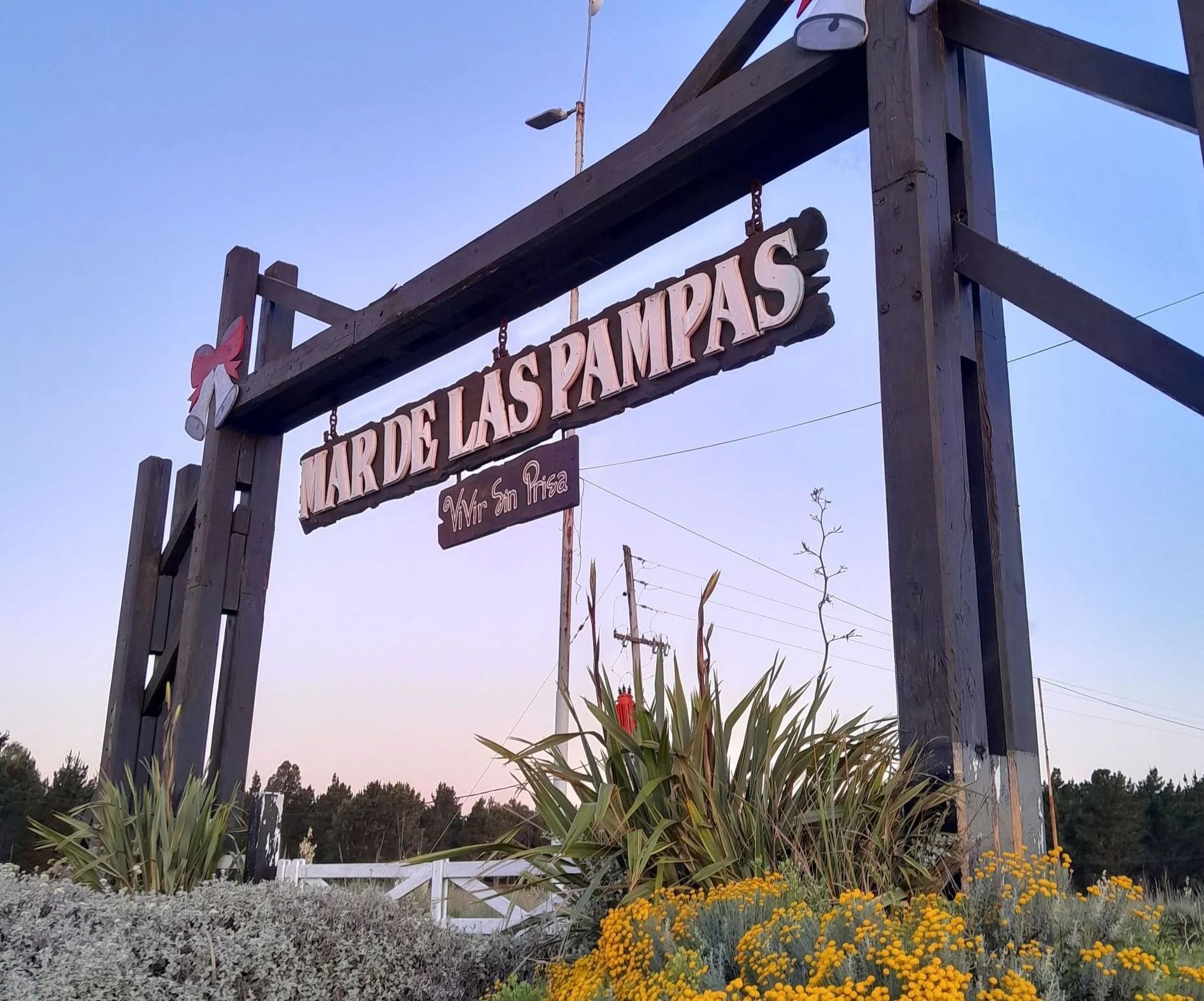 Un letrero de madera en la entrada dice “RUTA DE LAS PAMPAS” junto a flores al atardecer.