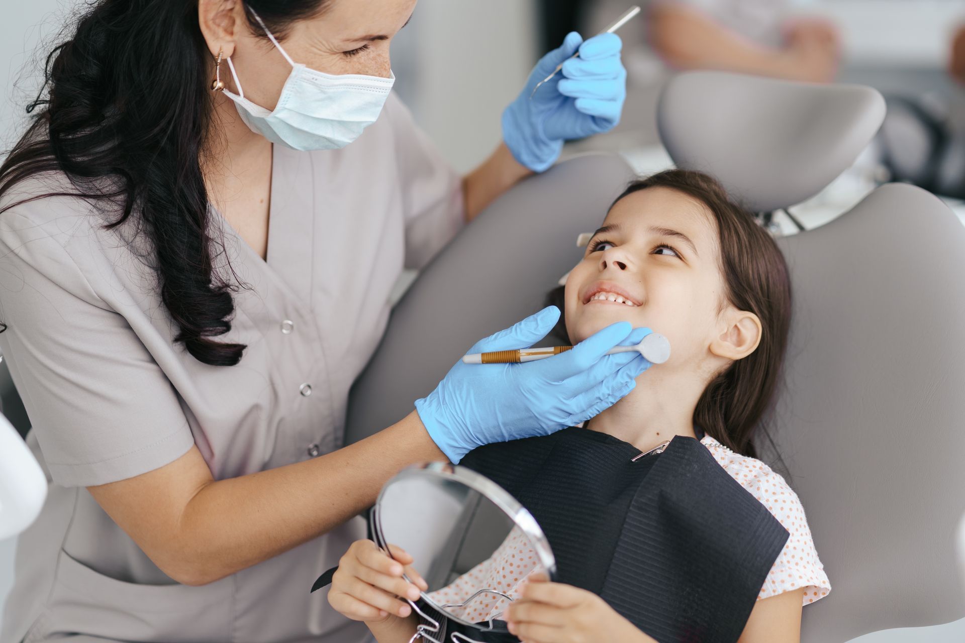 Dentista examinando a un niño sonriente en el sillón dental, con mascarilla y guantes azules.
