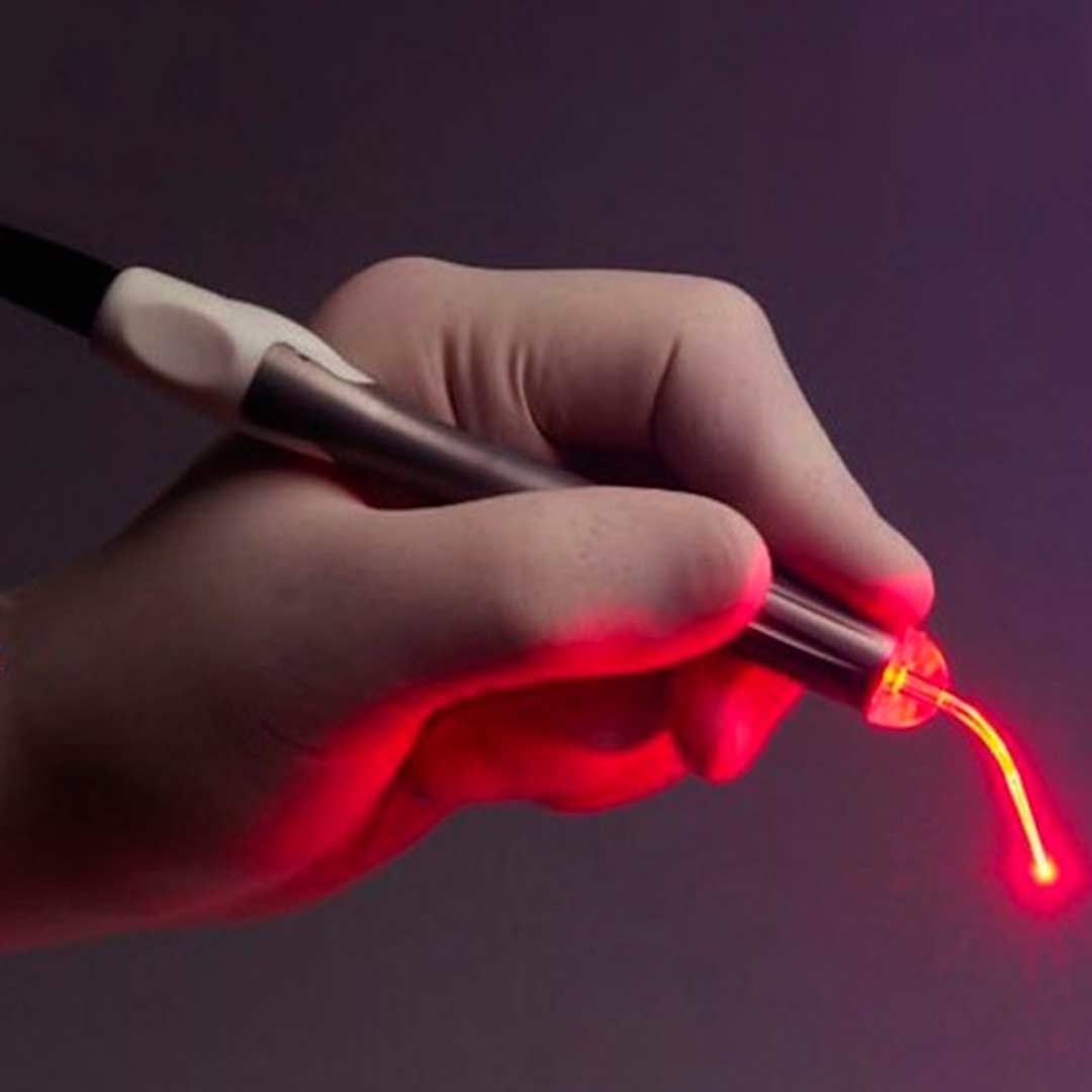 Mano sosteniendo un lápiz óptico de metal que brilla en rojo en la punta sobre un fondo oscuro.