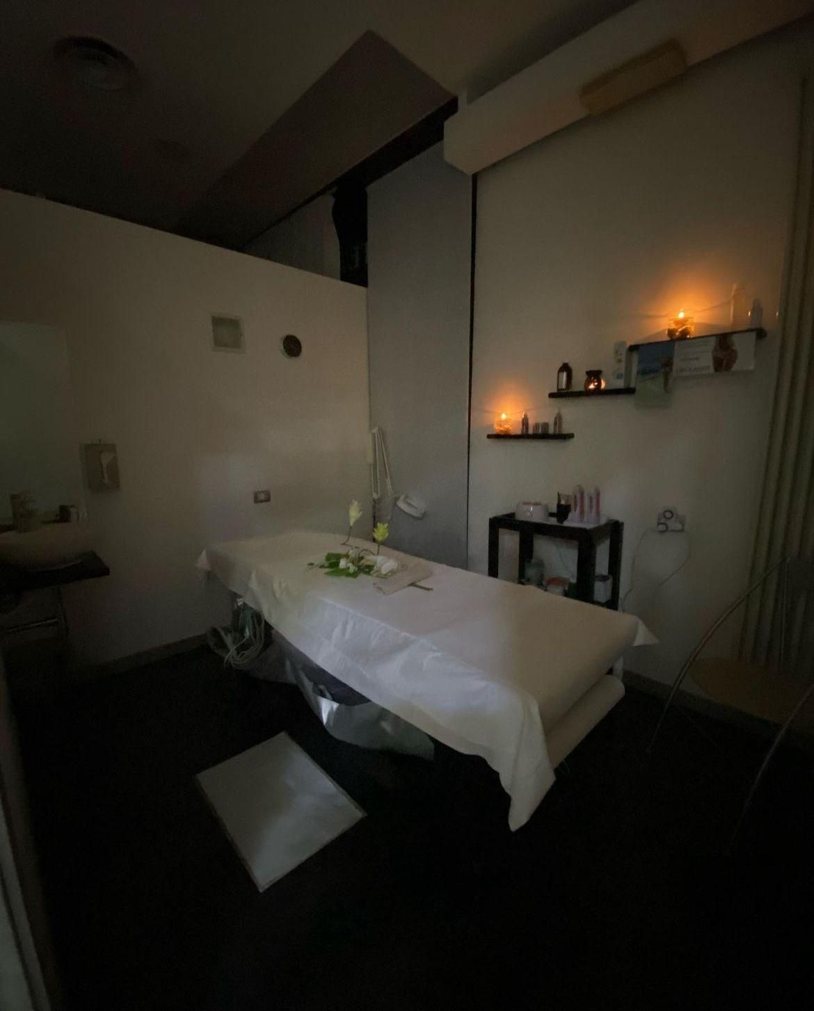 Un lettino per massaggi in una stanza buia con candele sugli scaffali.