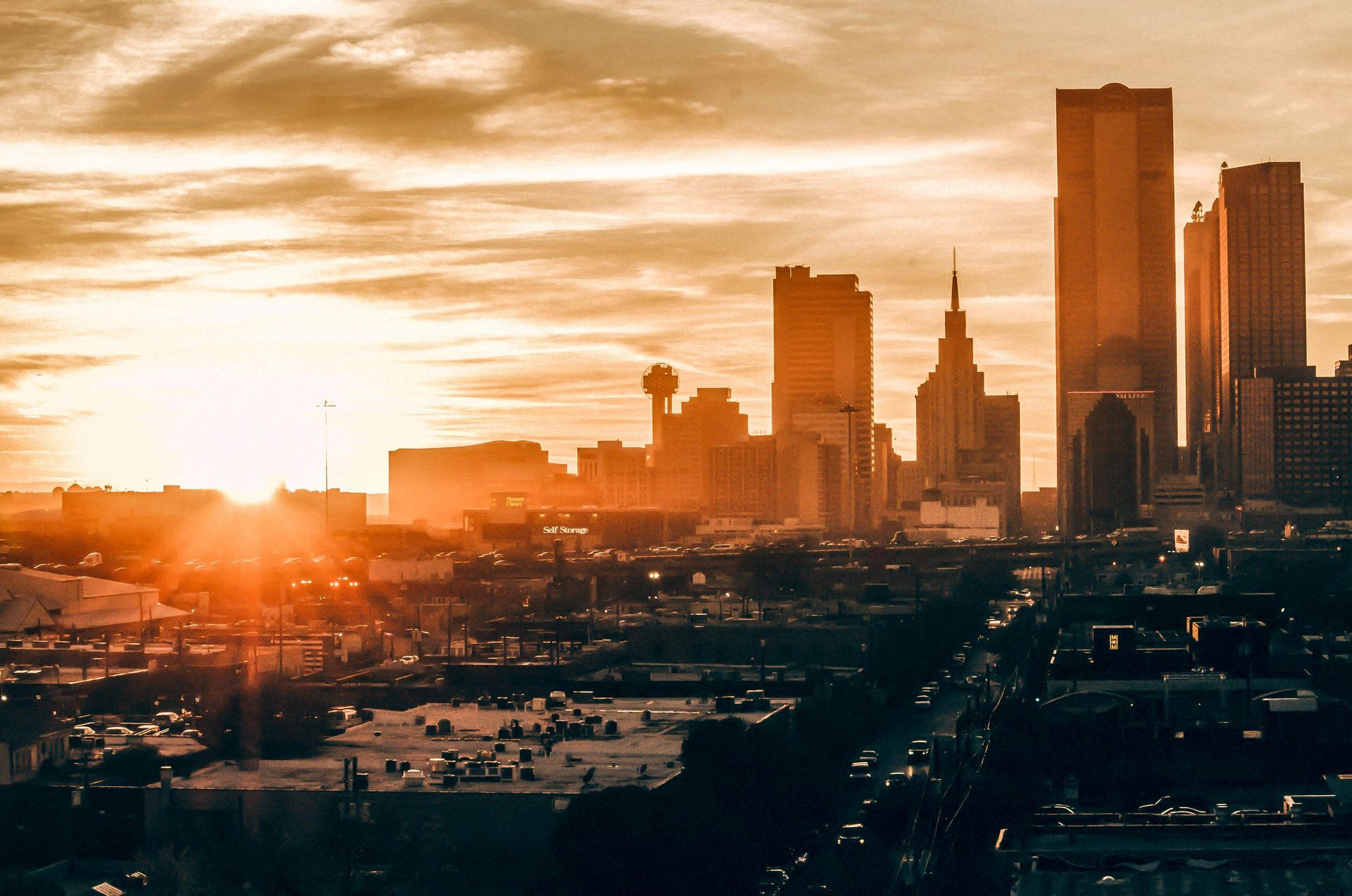 A city skyline at sunset with the sun shining through the clouds.