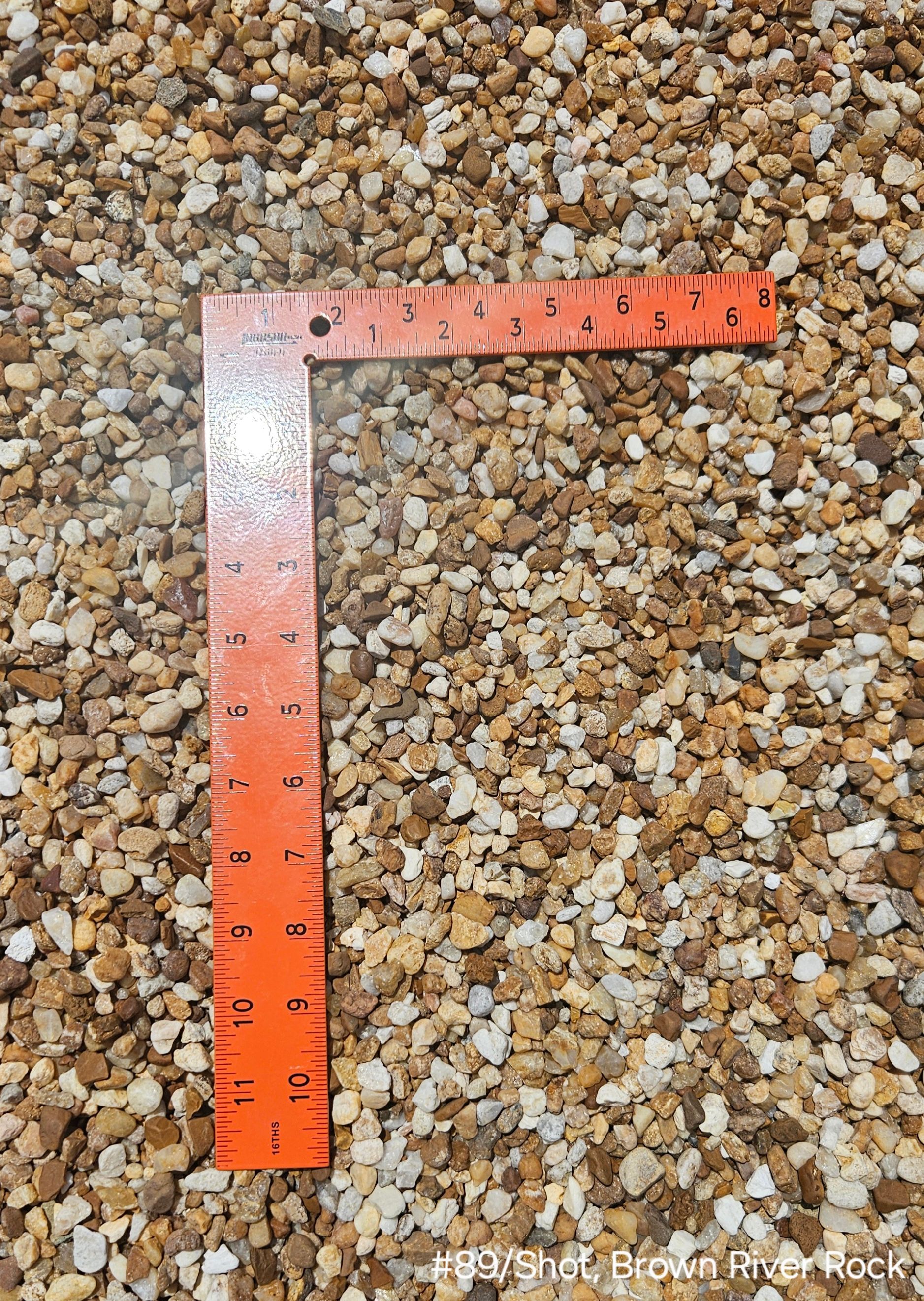 Orange square ruler on a bed of small, light-brown pebbles.
