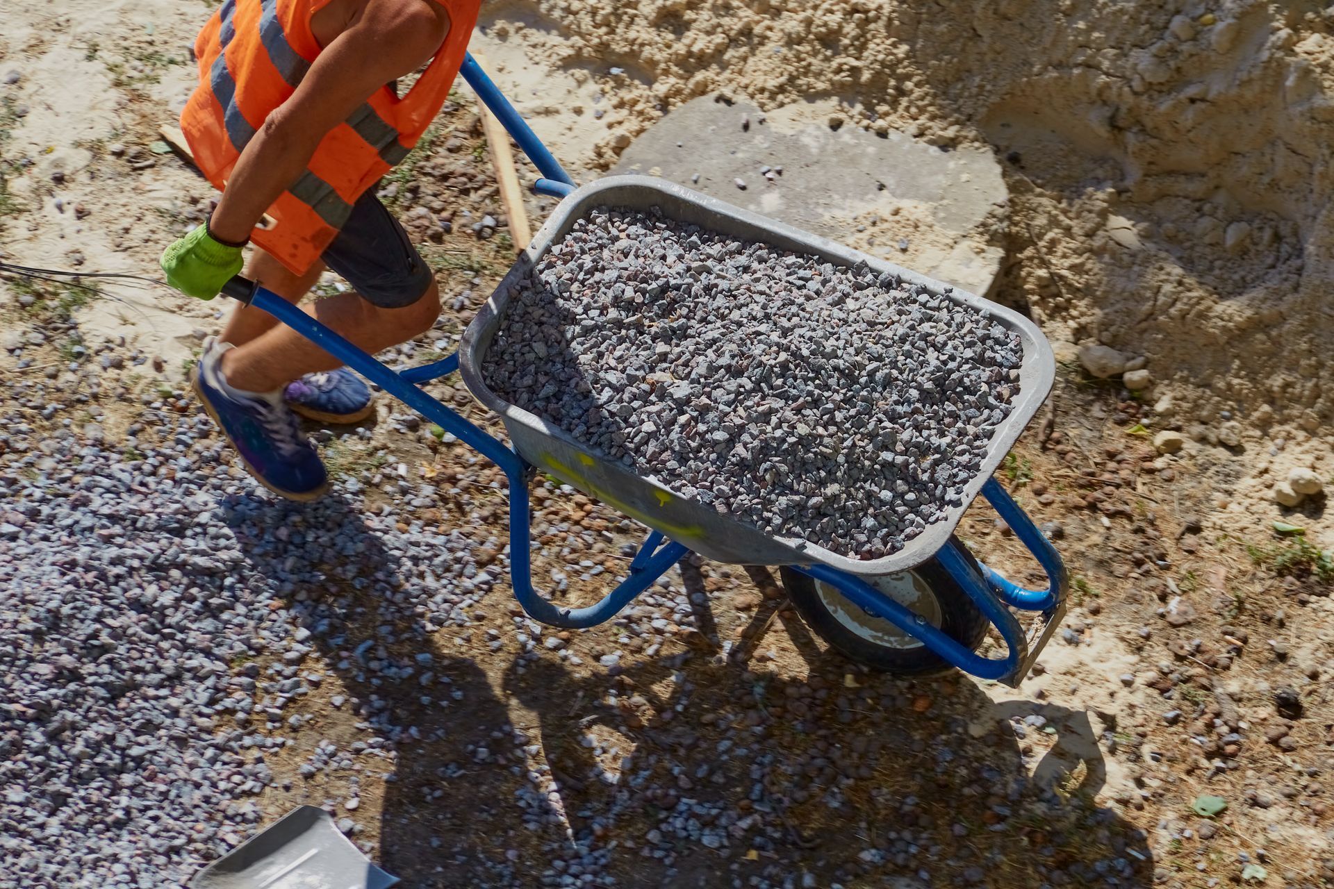 Construction worker pushing a wheelbarrow loaded with gravel across a dirt worksite.
