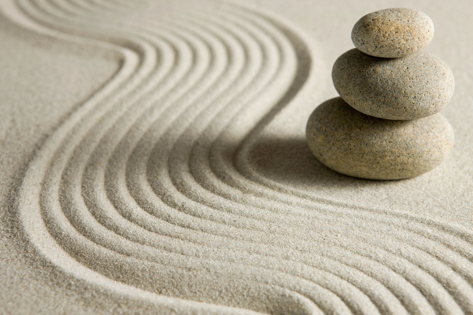Stacked smooth stones on raked sand with flowing patterns, creating a peaceful Zen garden scene.