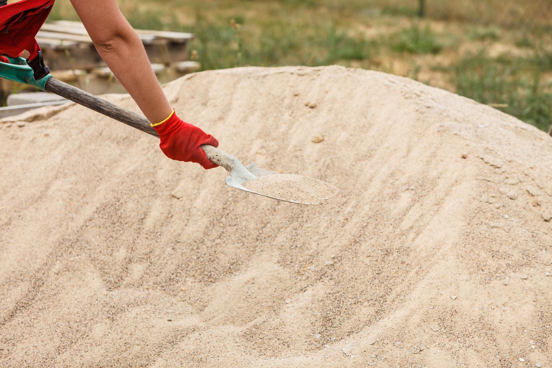 Person in red gloves spreading sand or cement with a trowel outdoors.