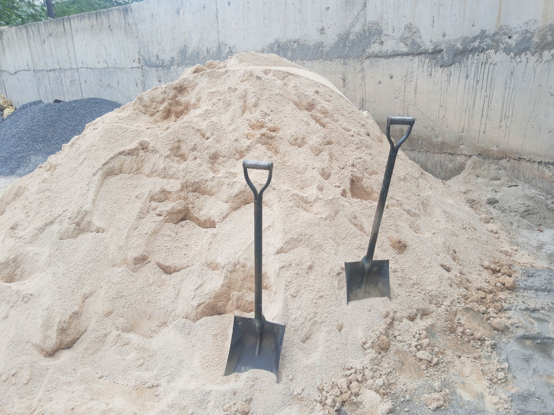 Two shovels stuck in a large pile of sand at a construction site.