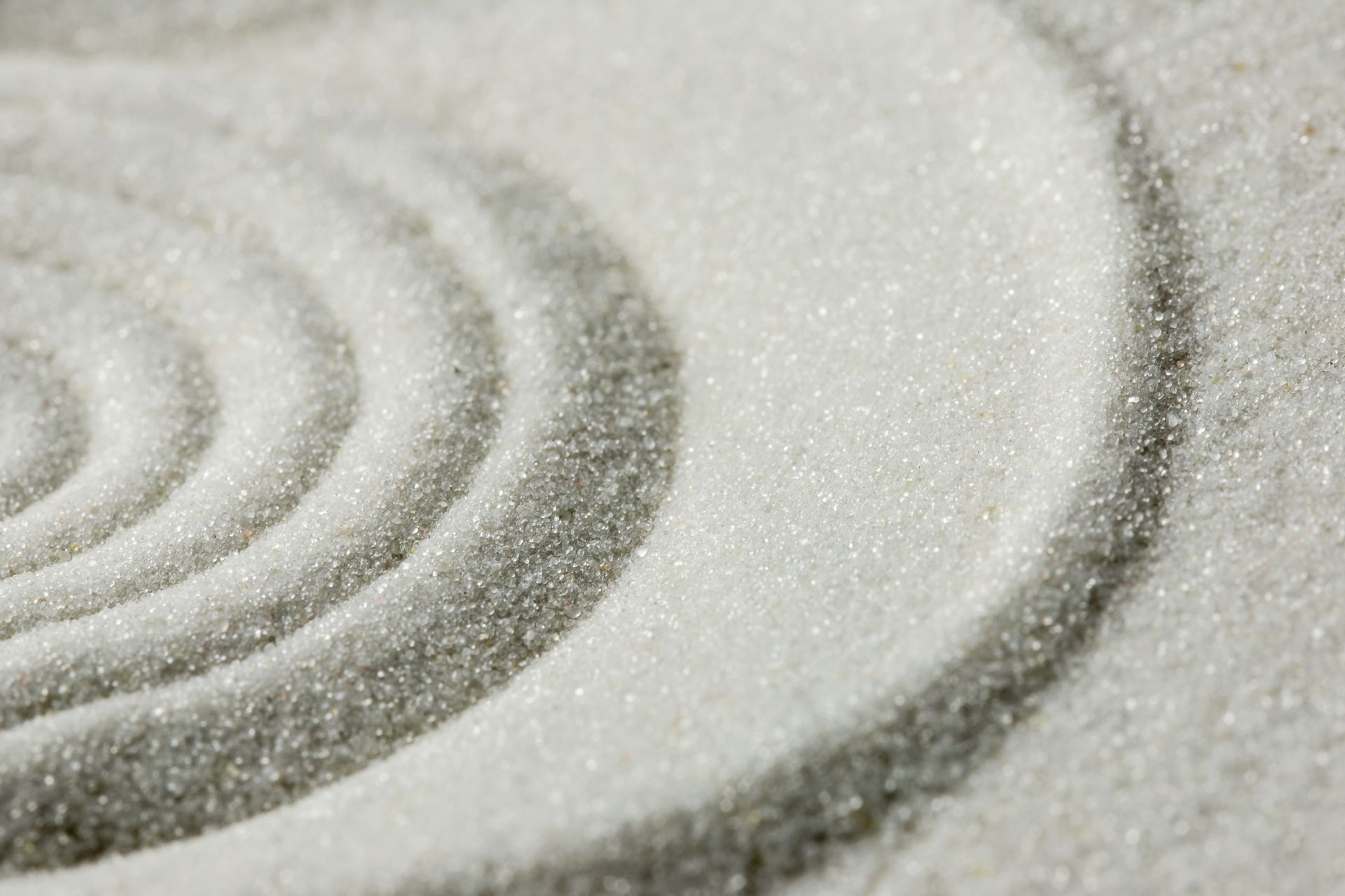 Close-up of white granulated material with curved rake patterns creating a textured surface. Close-up of white granulated material with curved rake patterns creating a textured surface.