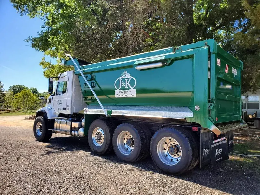 Green dump truck parked on gravel, with a white cab and logo.