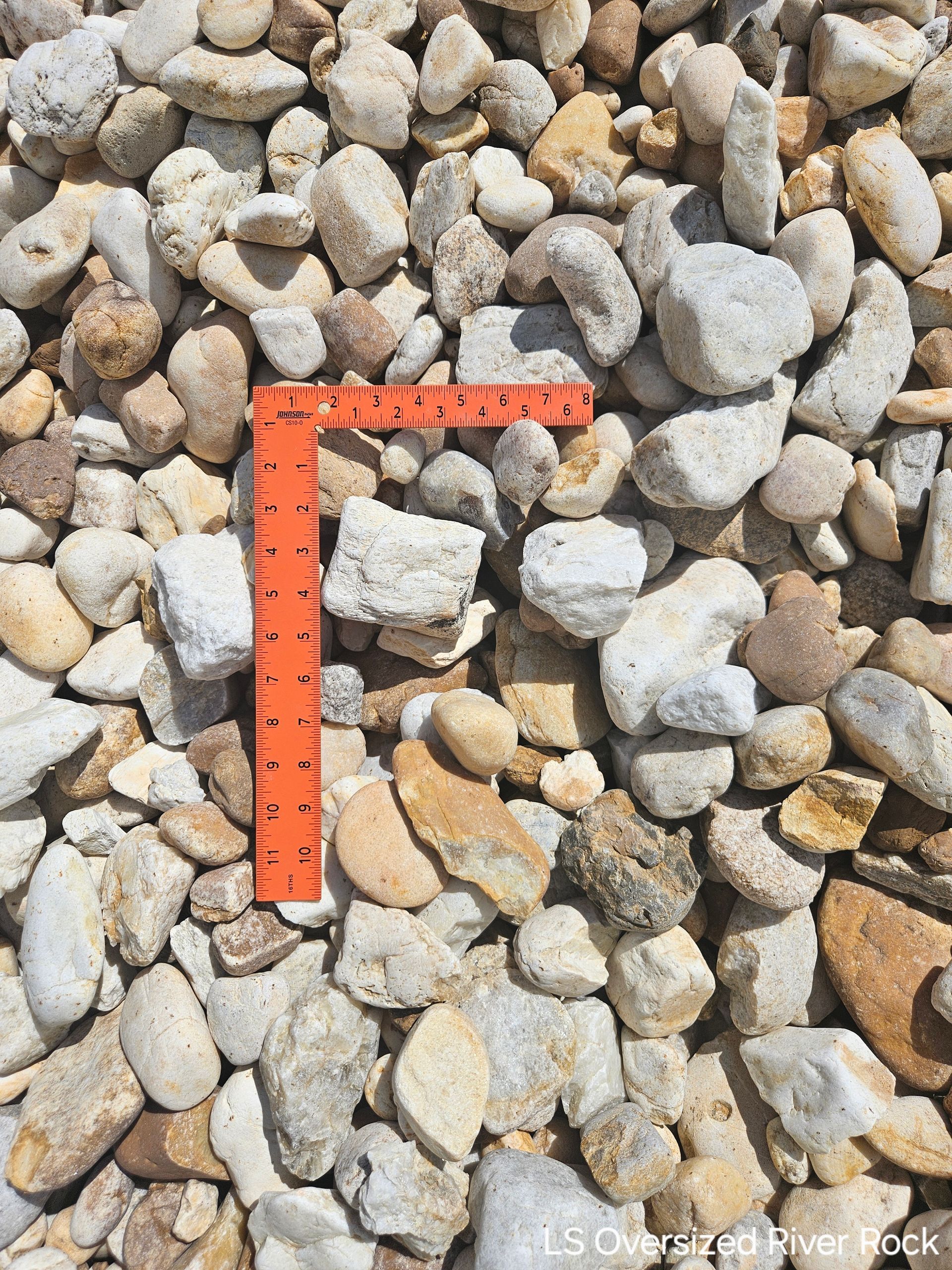 Overhead shot of a pile of light-colored, rounded river rocks with an orange ruler for scale.