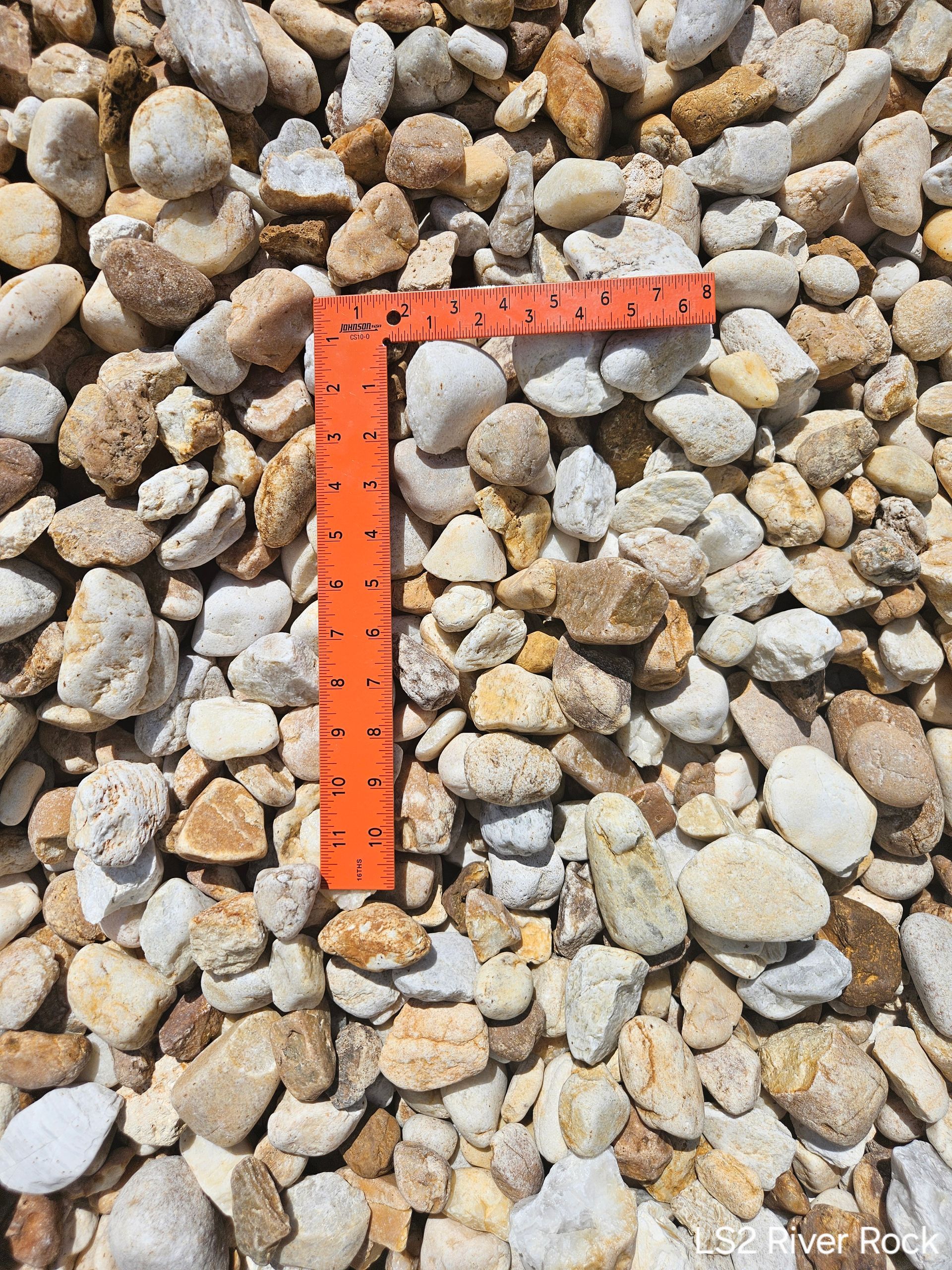 Pile of mixed-color river rock with an orange ruler placed on top for scale.