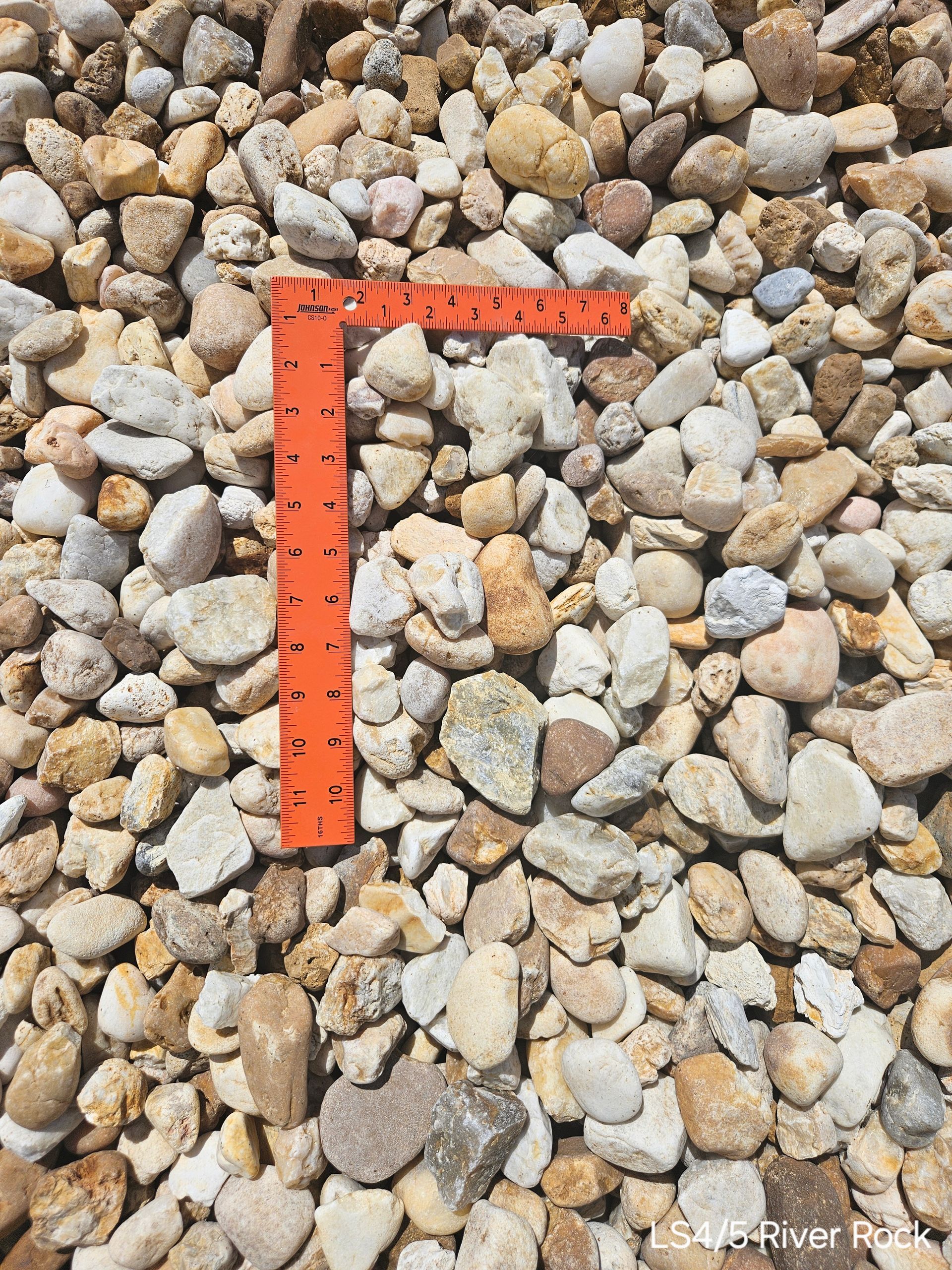 Close-up of gravel, various beige and off-white tones. An orange ruler is placed among the rocks.