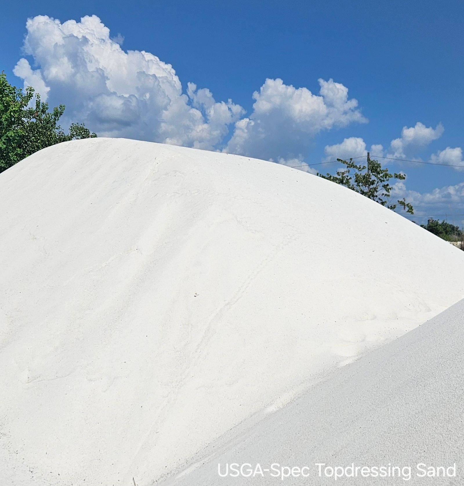 White sand pile under a blue sky with clouds; labeled