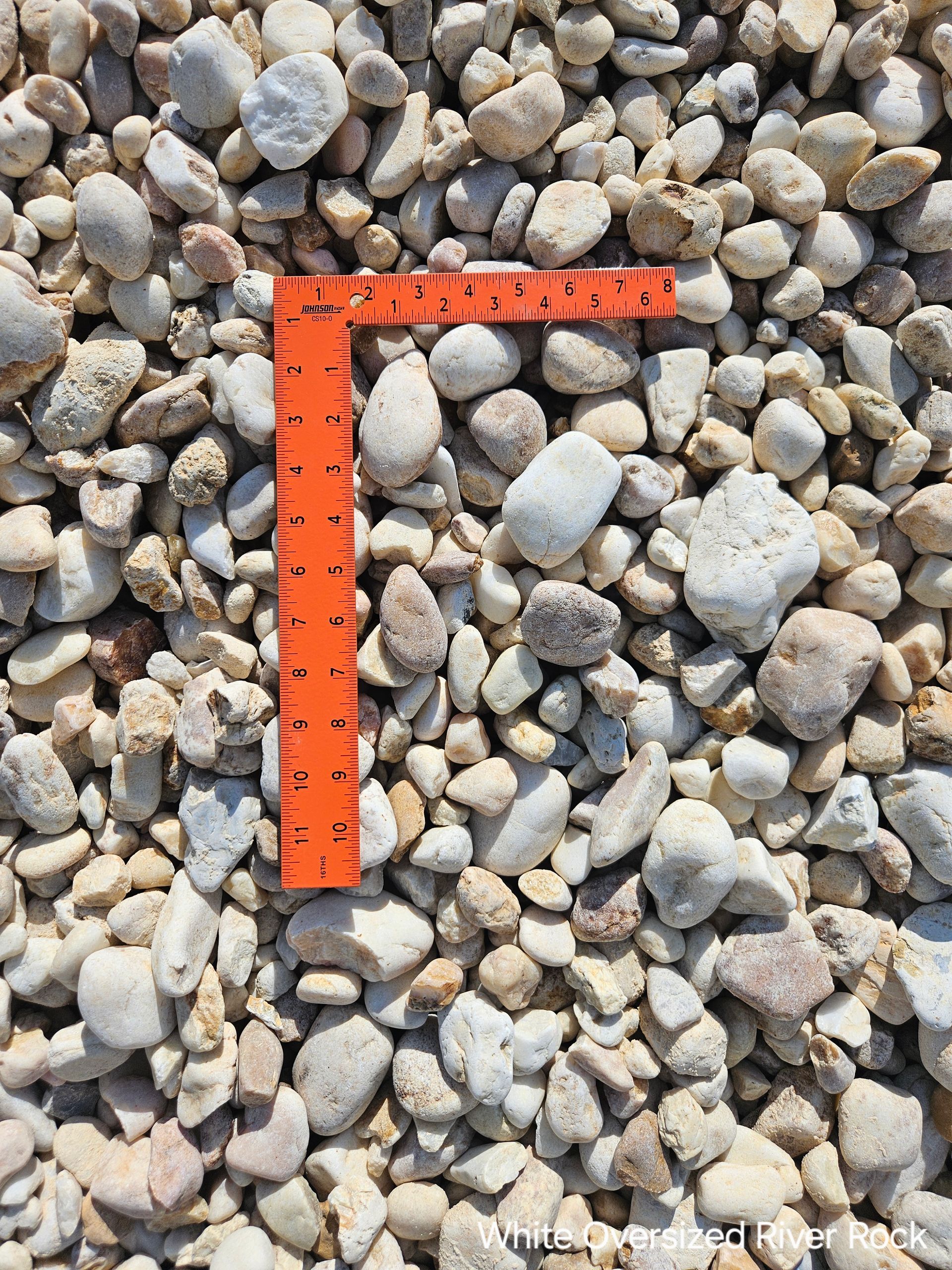 Tan and white river rock gravel with an orange ruler for scale.
