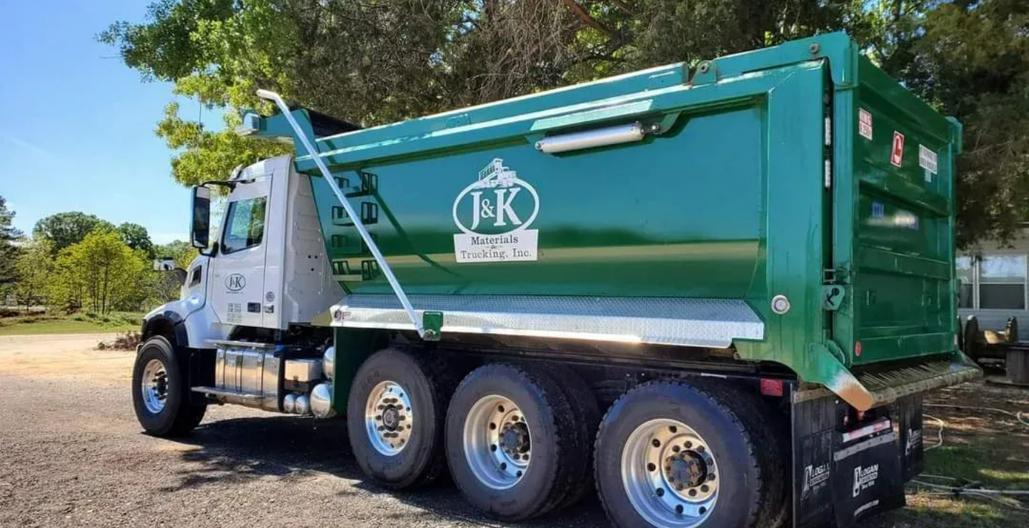 A truck from J & K Materials & Trucking is below a tree, at daylight. A truck from J & K Materials & Trucking is below a tree, at daylight.