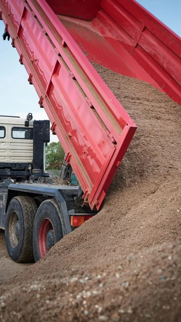 A construction truck dumps a pile of fine earth on the ground. A construction truck dumps a pile of fine earth on the ground.