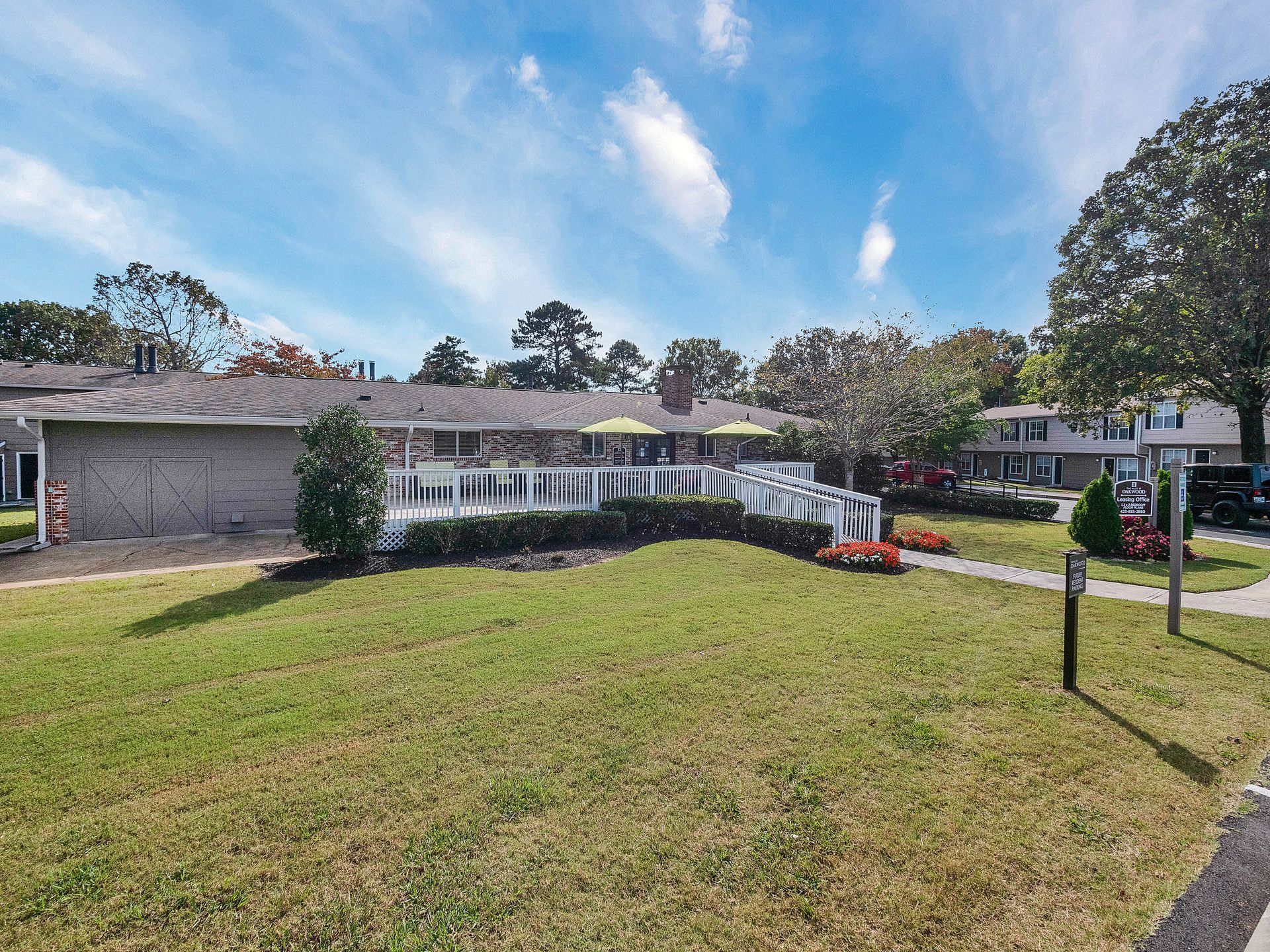 A sprawling one-story brick house with a large, white-fenced patio and a manicured lawn under a sunny, blue sky.