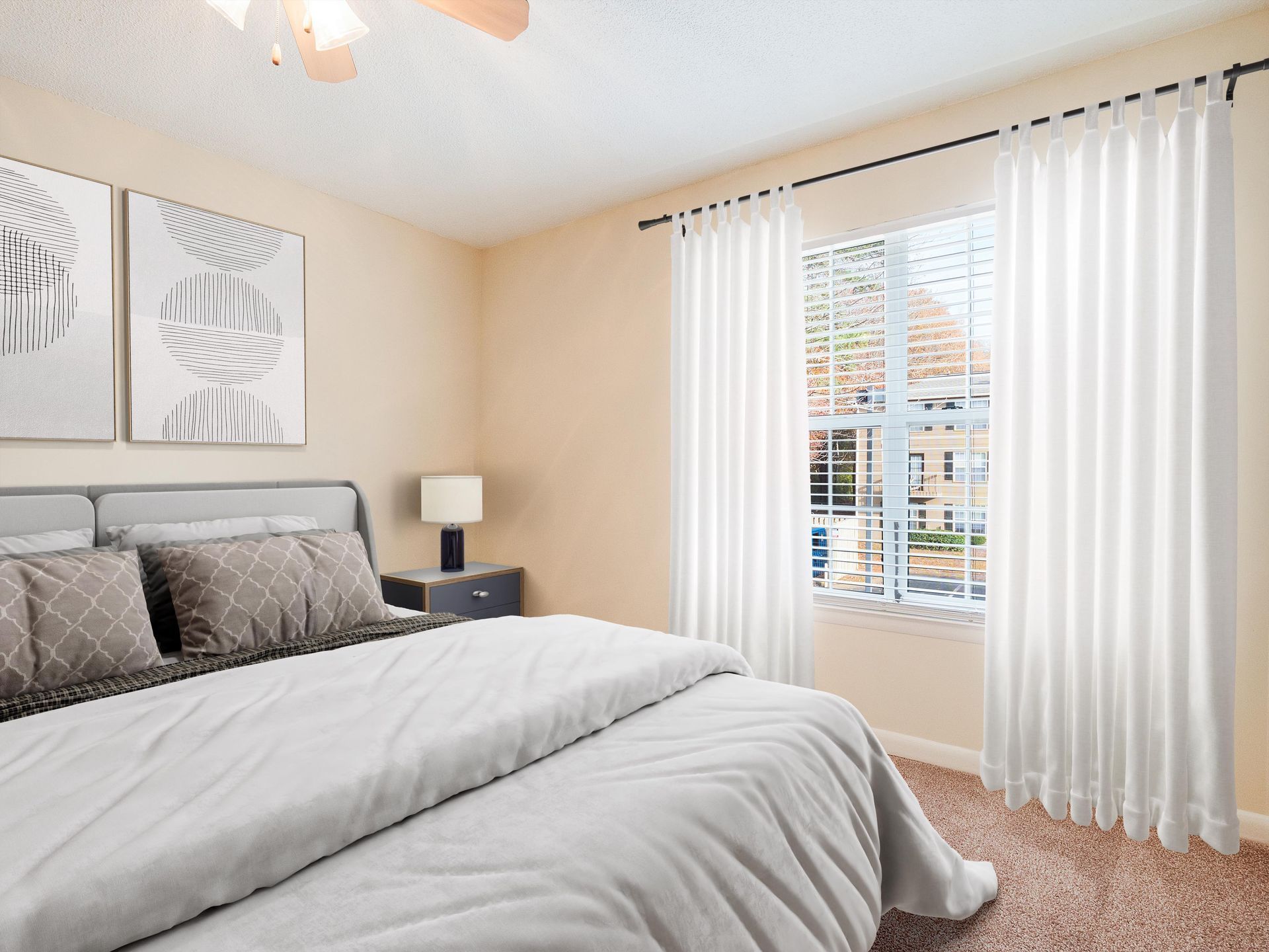 A bedroom featuring a bed with gray bedding, two abstract art prints on the wall, and white curtains by a window.