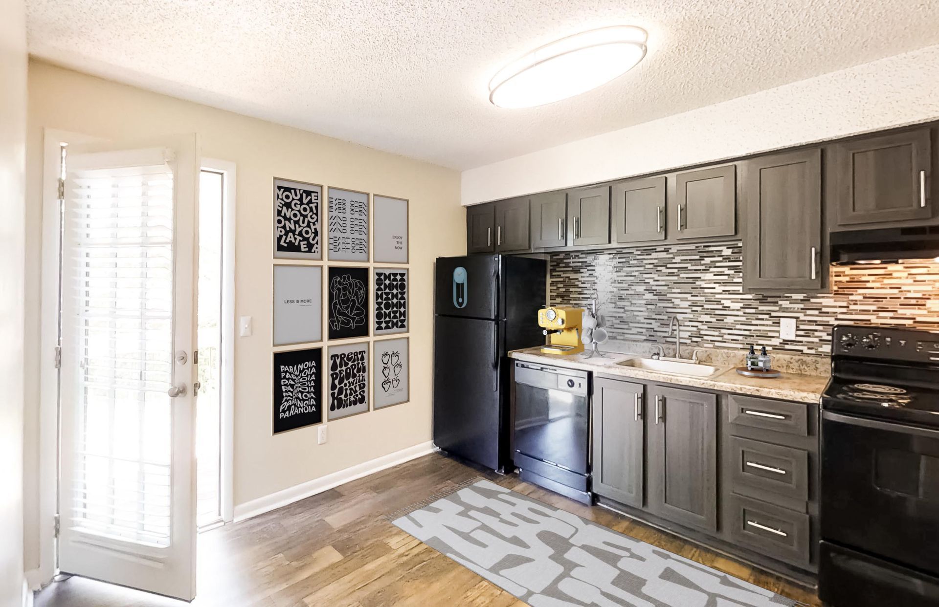 A kitchen featuring dark wood cabinets, black appliances, a textured backsplash, and wall art in an open floor plan.