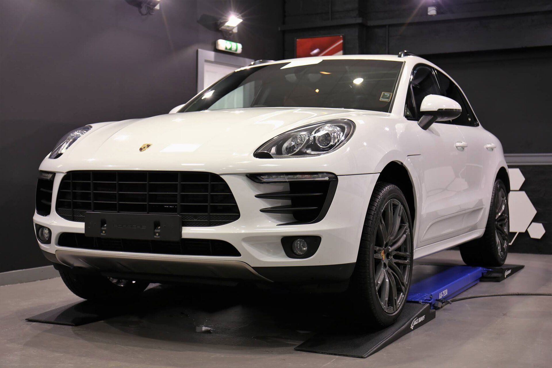 White Porsche SUV on a display platform in an indoor showroom, front angled view