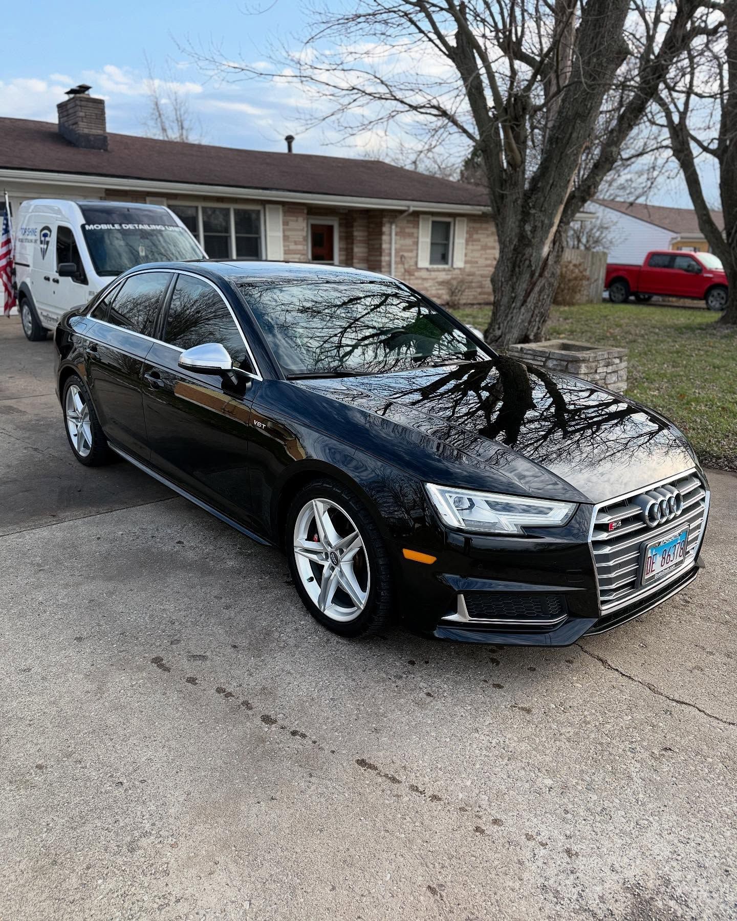Black Audi sedan parked in a driveway in front of a house.