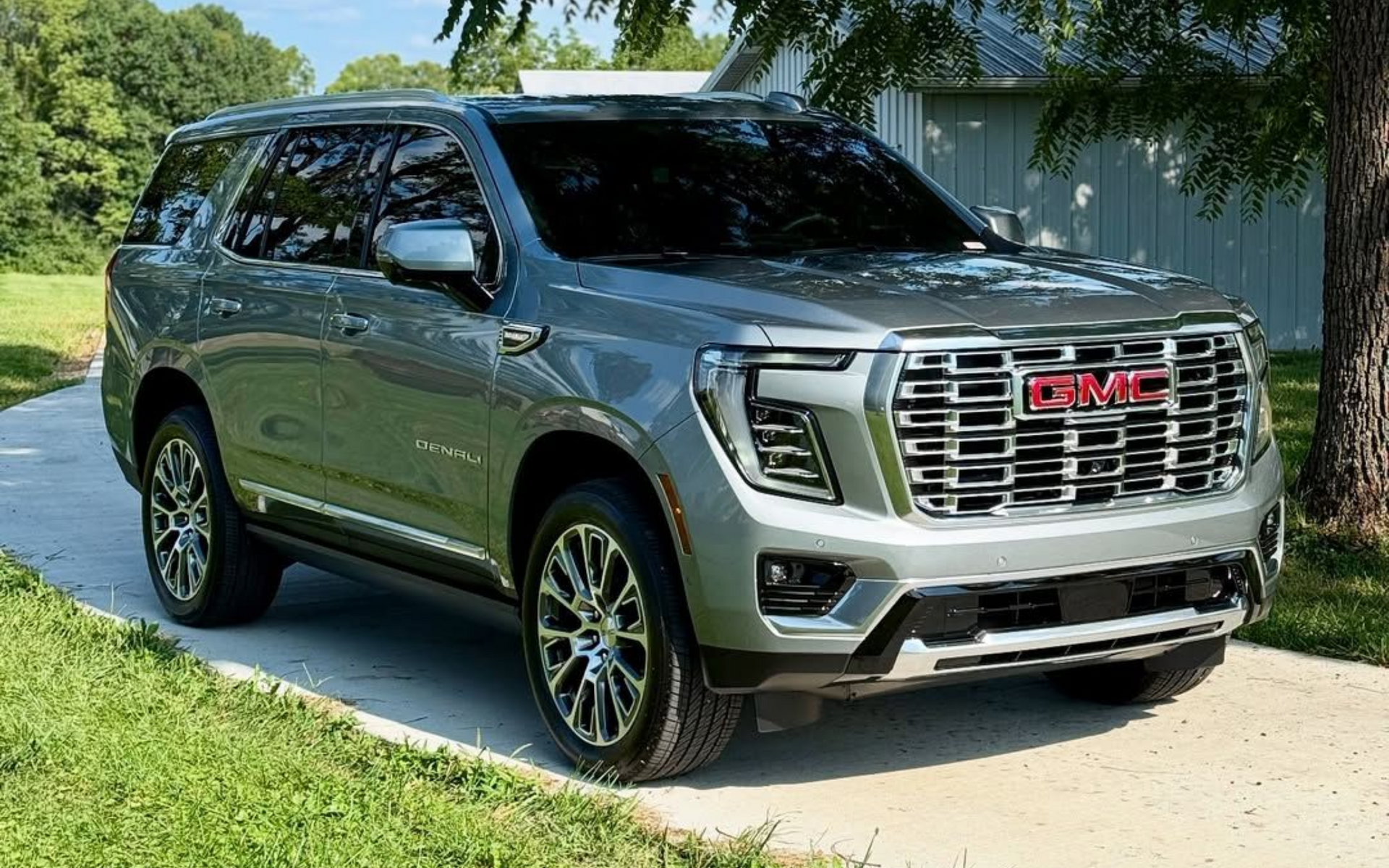 Gray GMC Yukon SUV parked on a driveway with a green lawn and tree in the background.