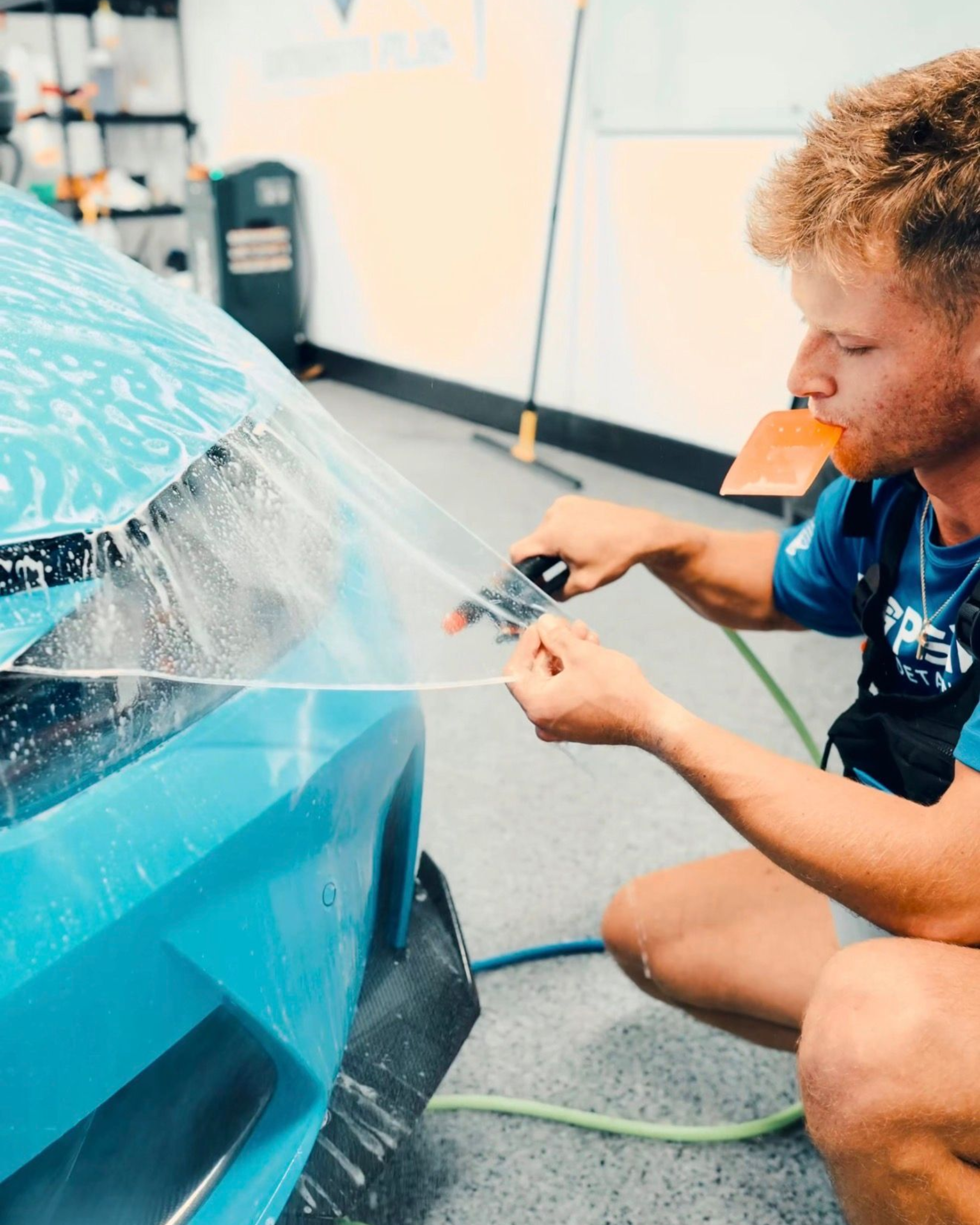 Person applying a blue film to a car body in a workshop