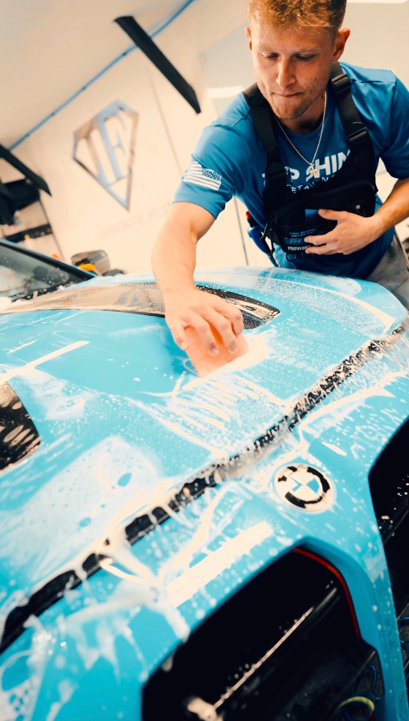 Person cleaning a blue race car hood with a cloth in a garage