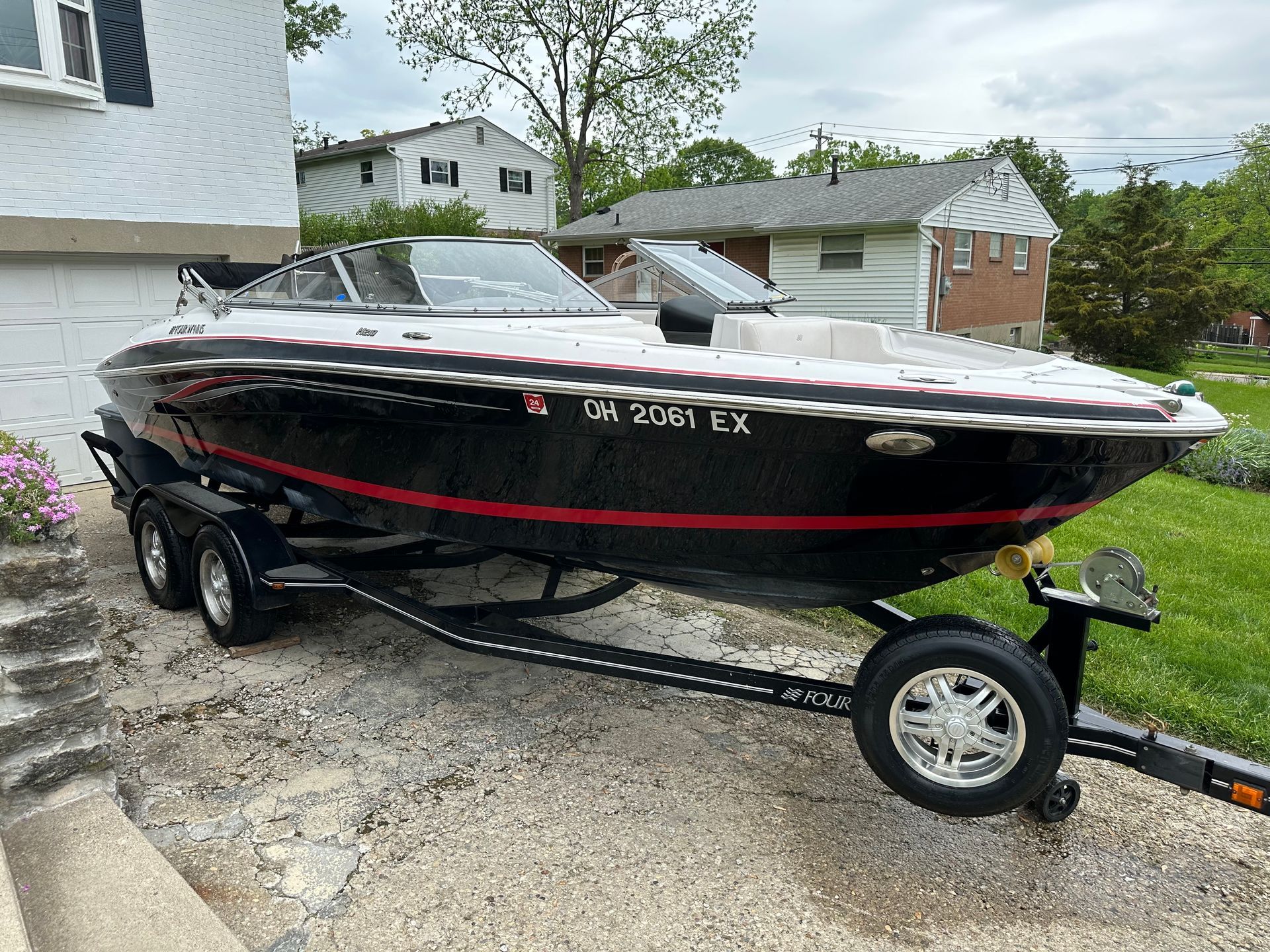 Black and red boat on a trailer parked in a driveway beside a house
