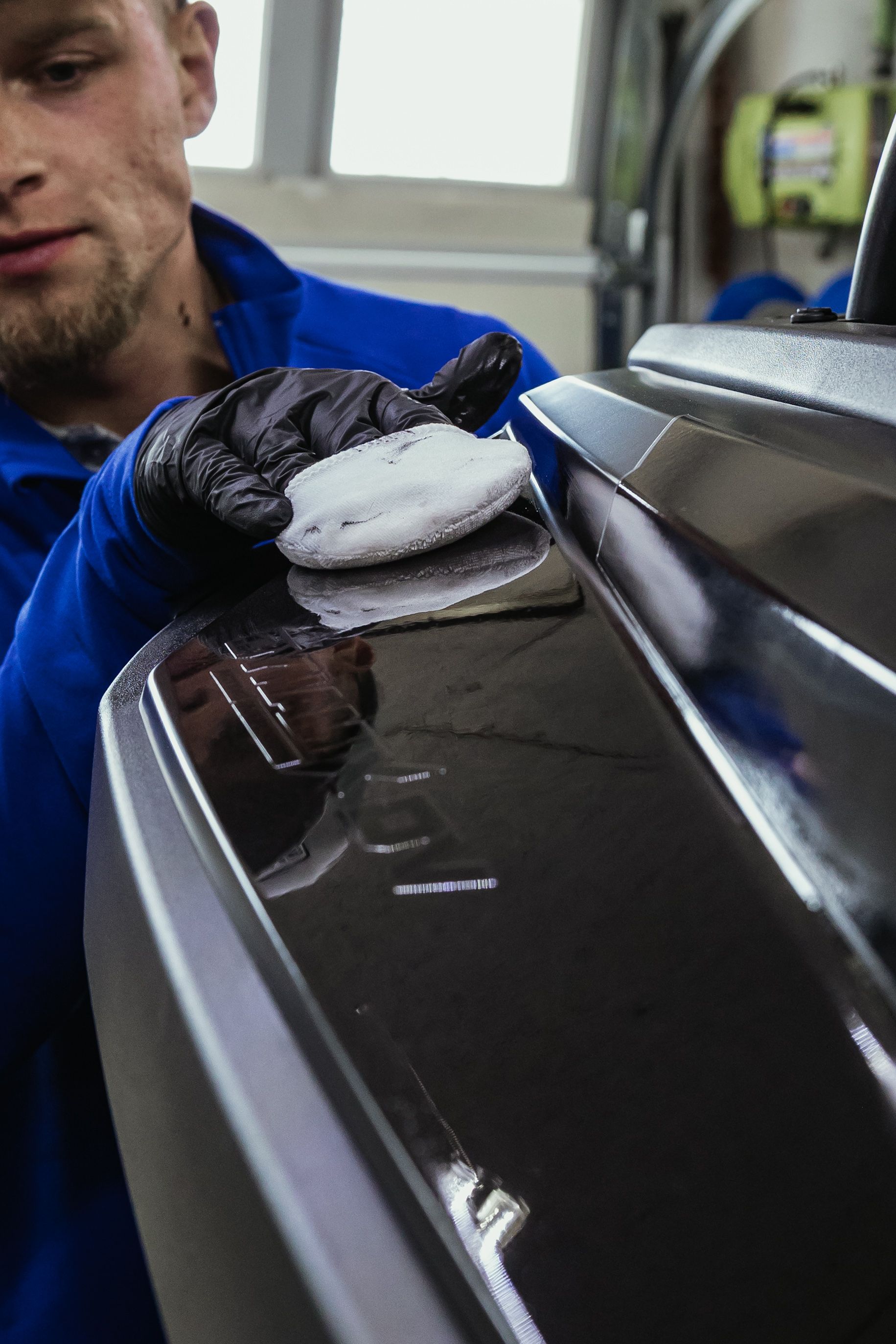 Gloved hand polishing a glossy black car panel with a white cloth in a garage