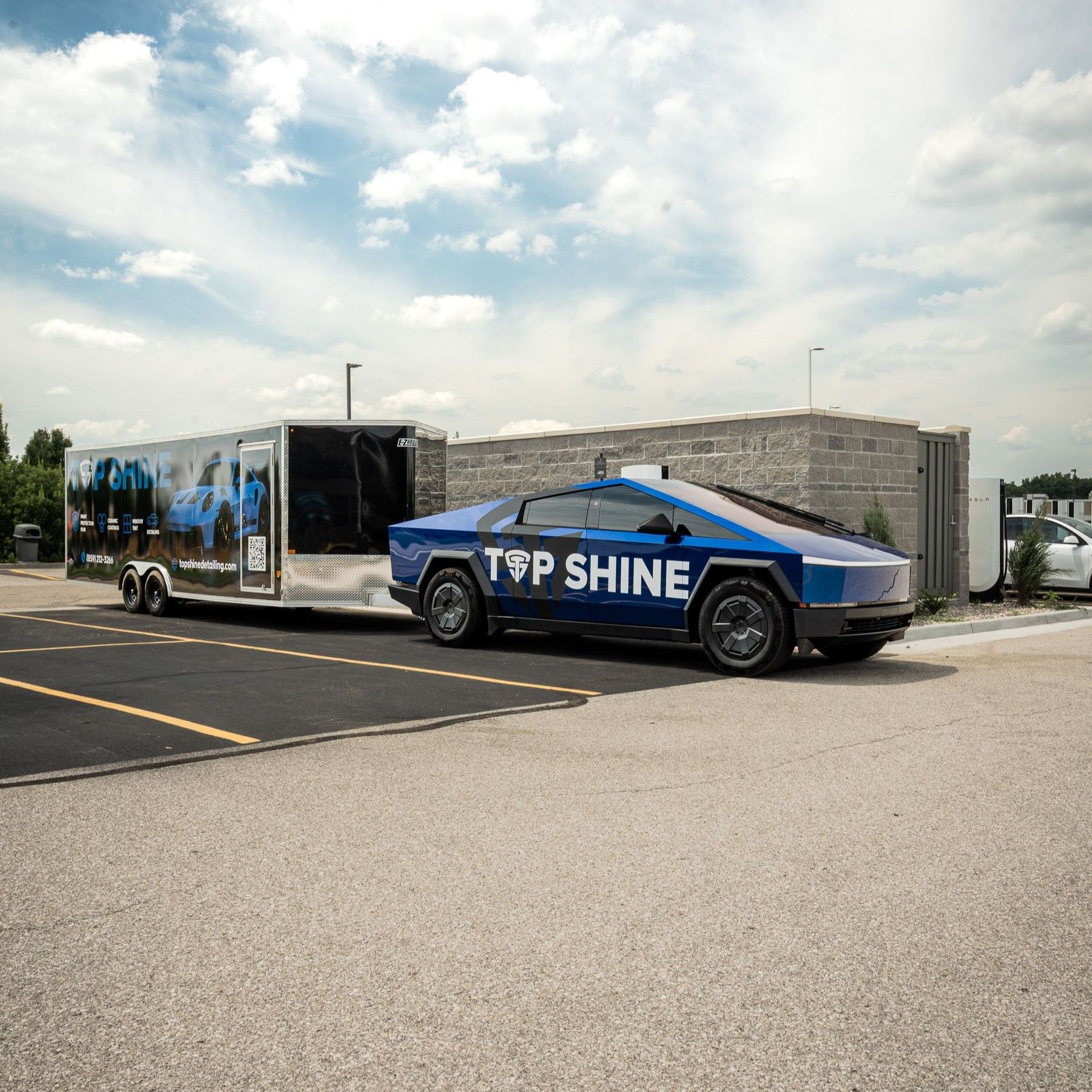 Blue “TSP SHINE” car hauling a branded trailer in a parking lot under a cloudy sky
