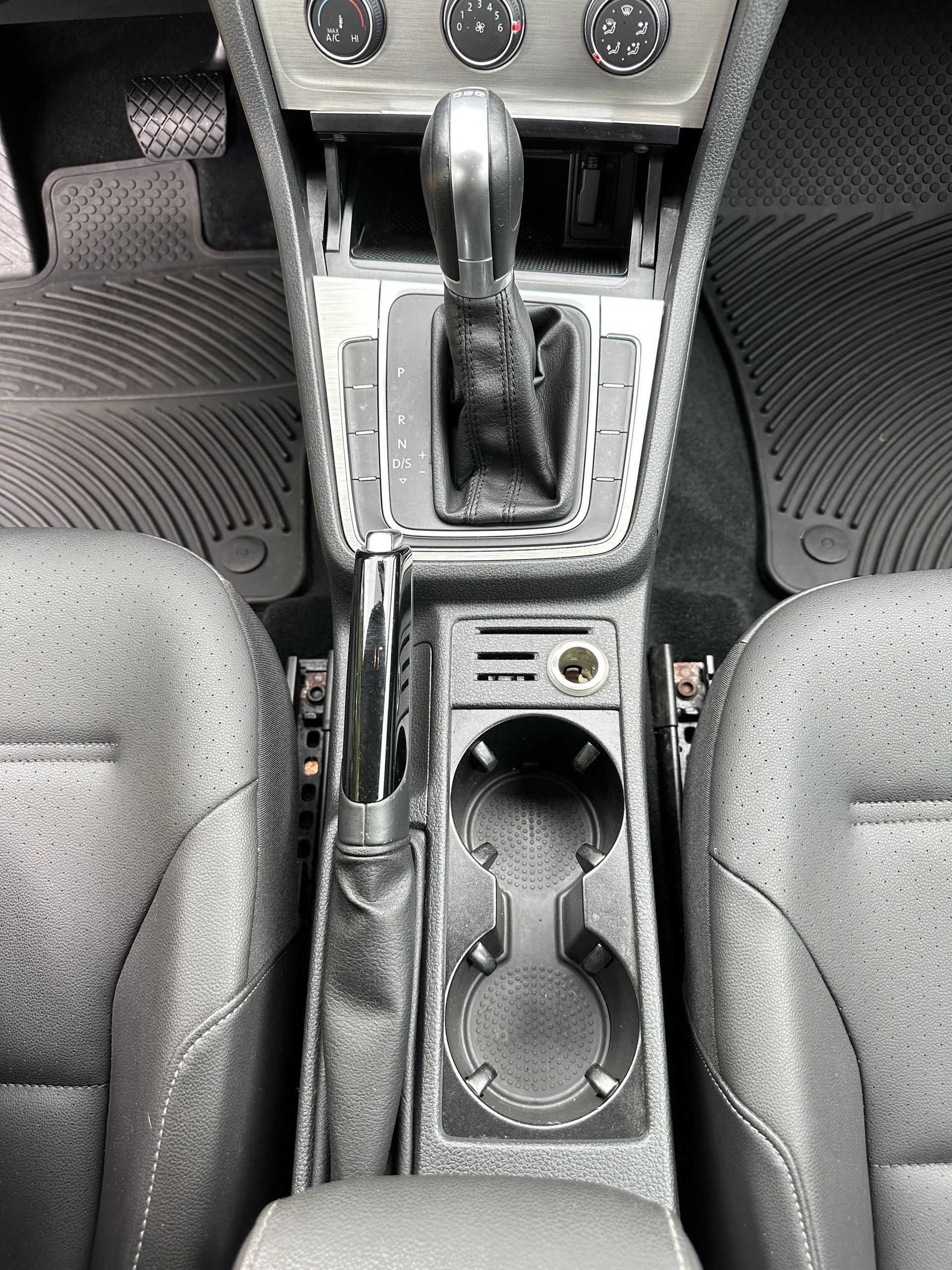 Car interior center console with gear shift, cup holders, and worn black trim.