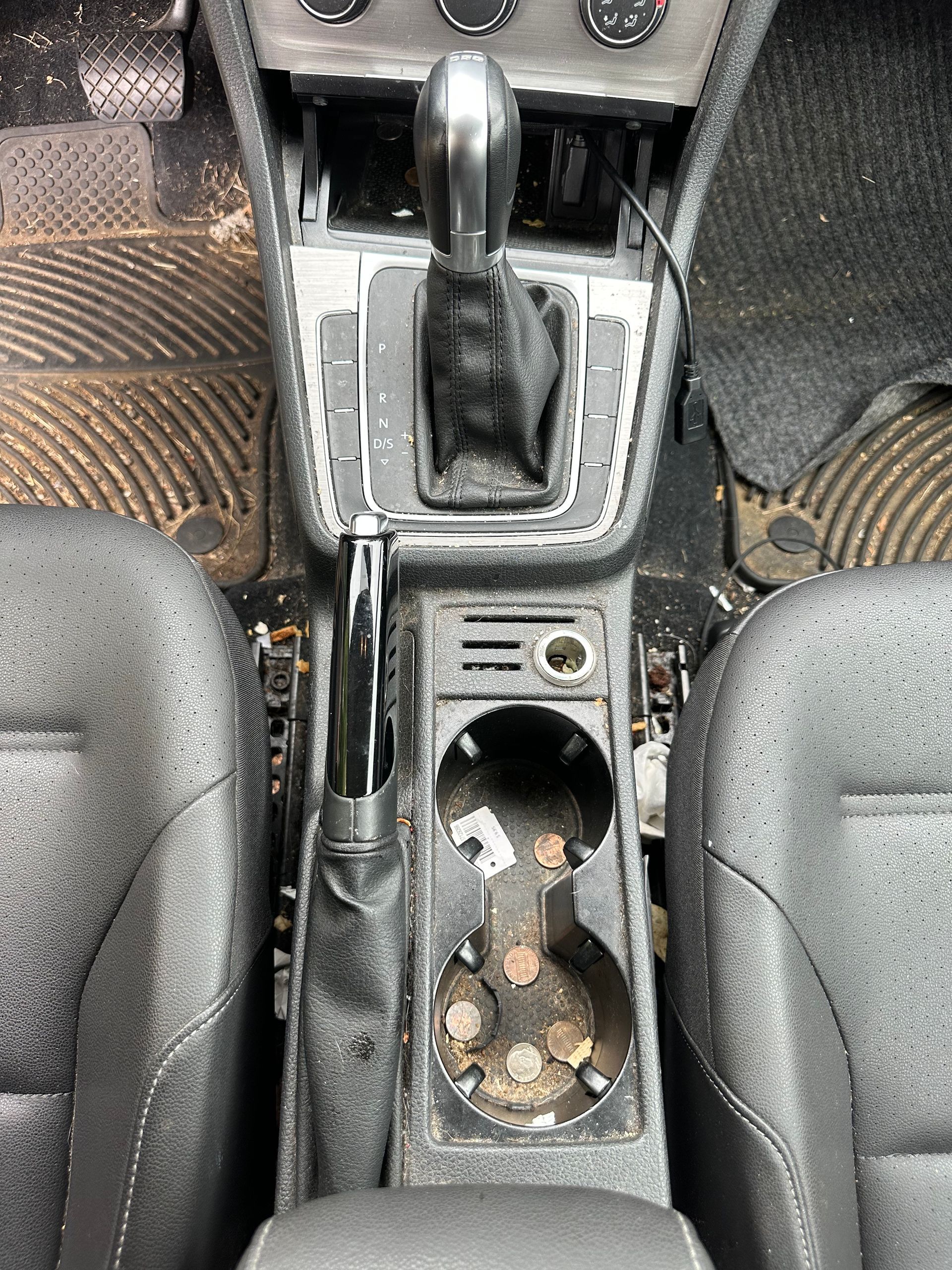 Car interior center console with gear shifter, handbrake, and open cup holder with coins and small items