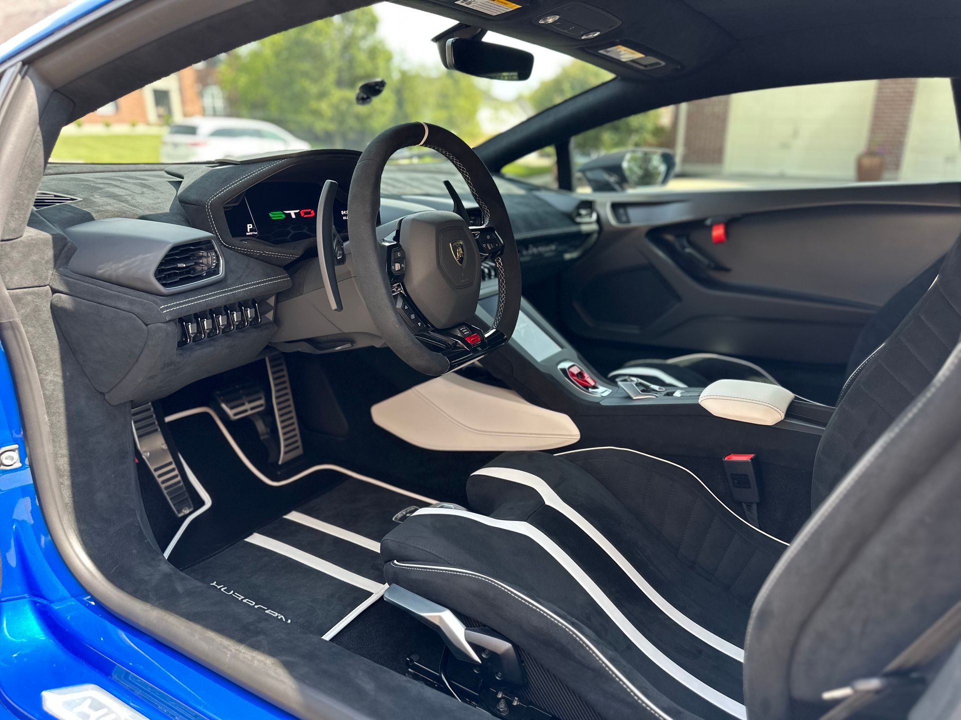 Interior view of a blue Lamborghini featuring black seats with white stripes, a black steering wheel, and custom floor mats.