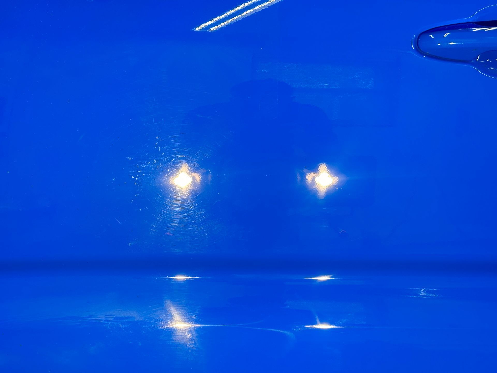 Blue car front with two bright headlights reflected on a glossy surface