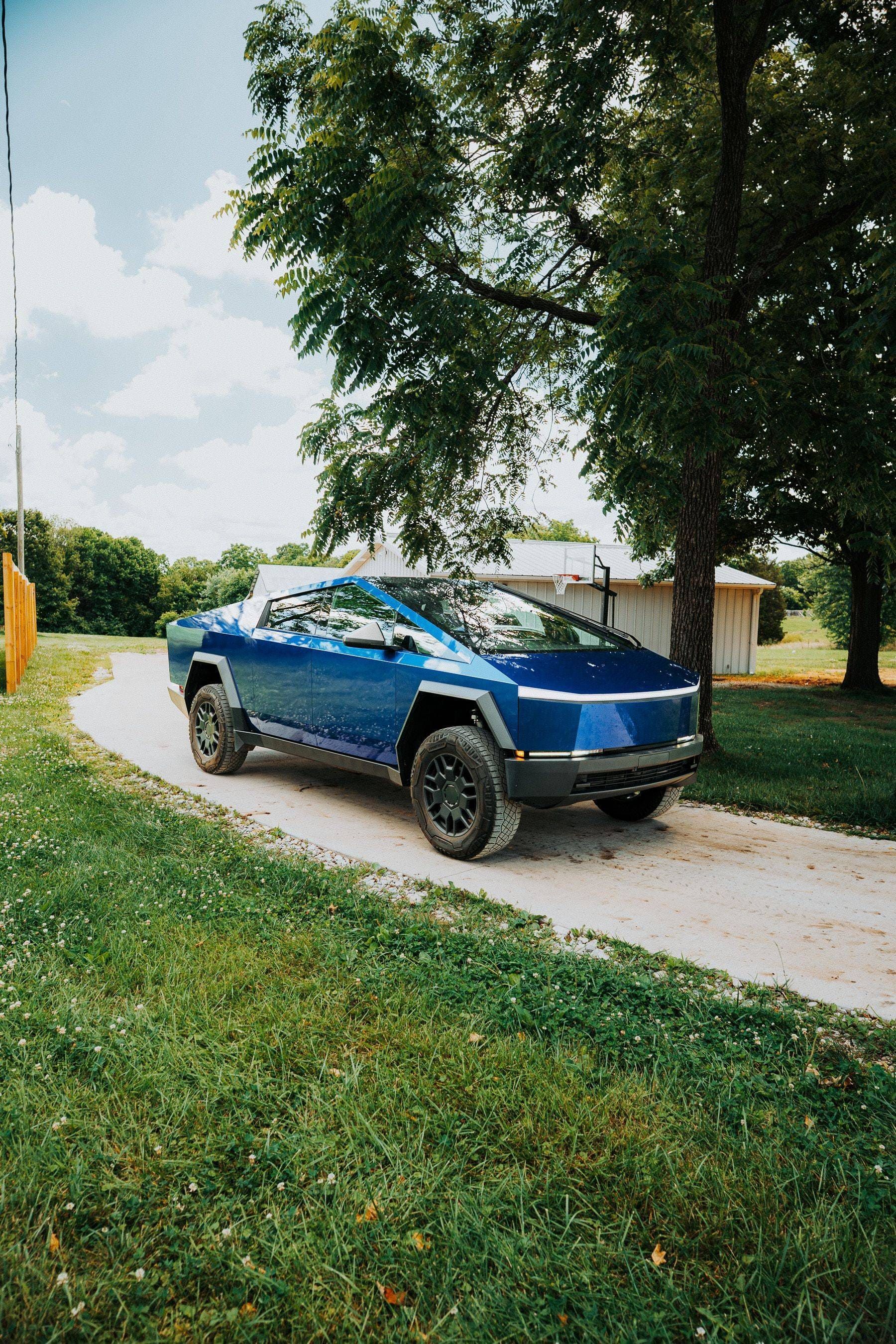 Blue tesla on a curved driveway beside a grassy lawn and trees