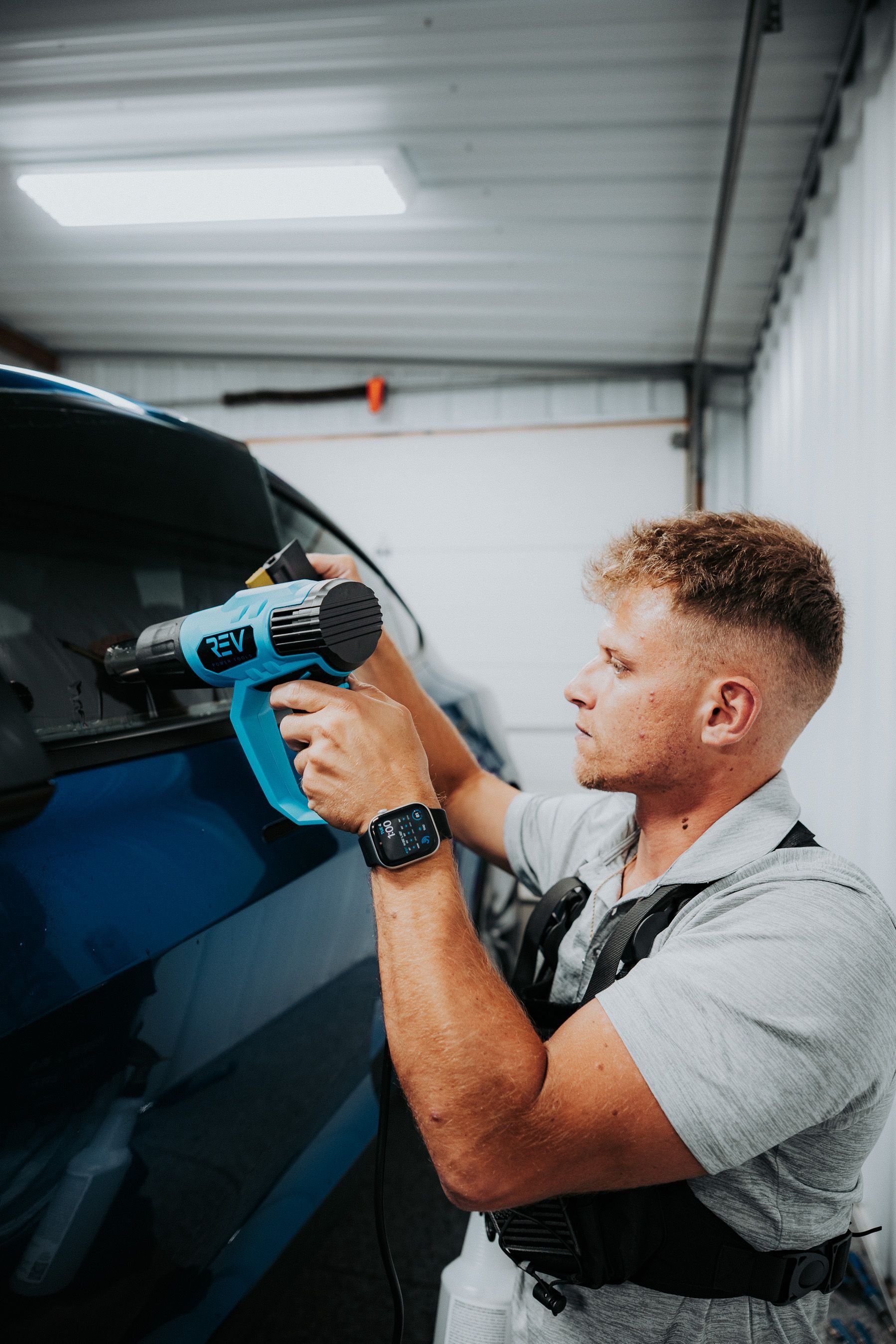 Worker using a blue power drill on a car in a garage